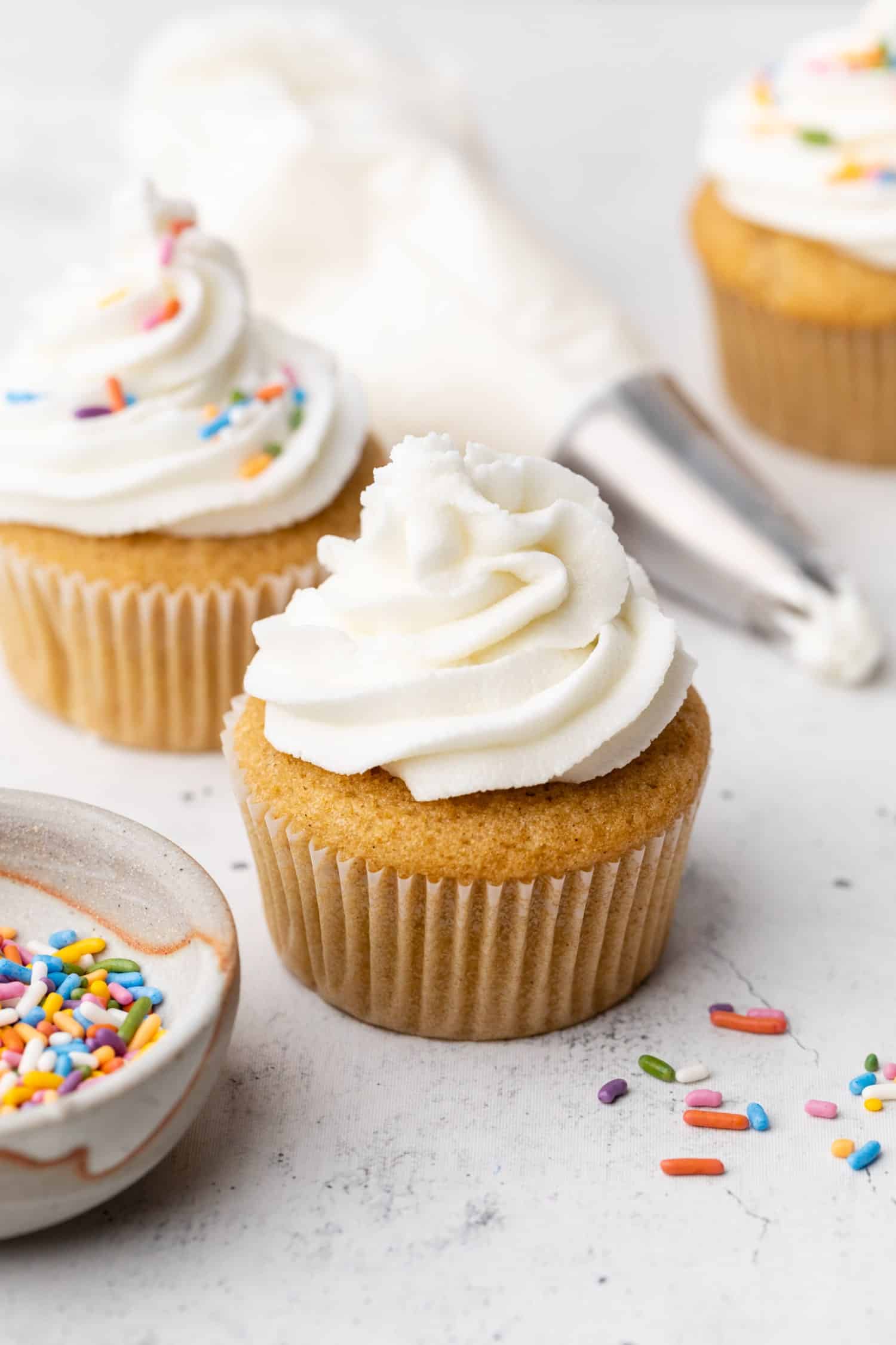 A pipping bag with dairy free frosting laying next to a cupcake with the frosting on top. 