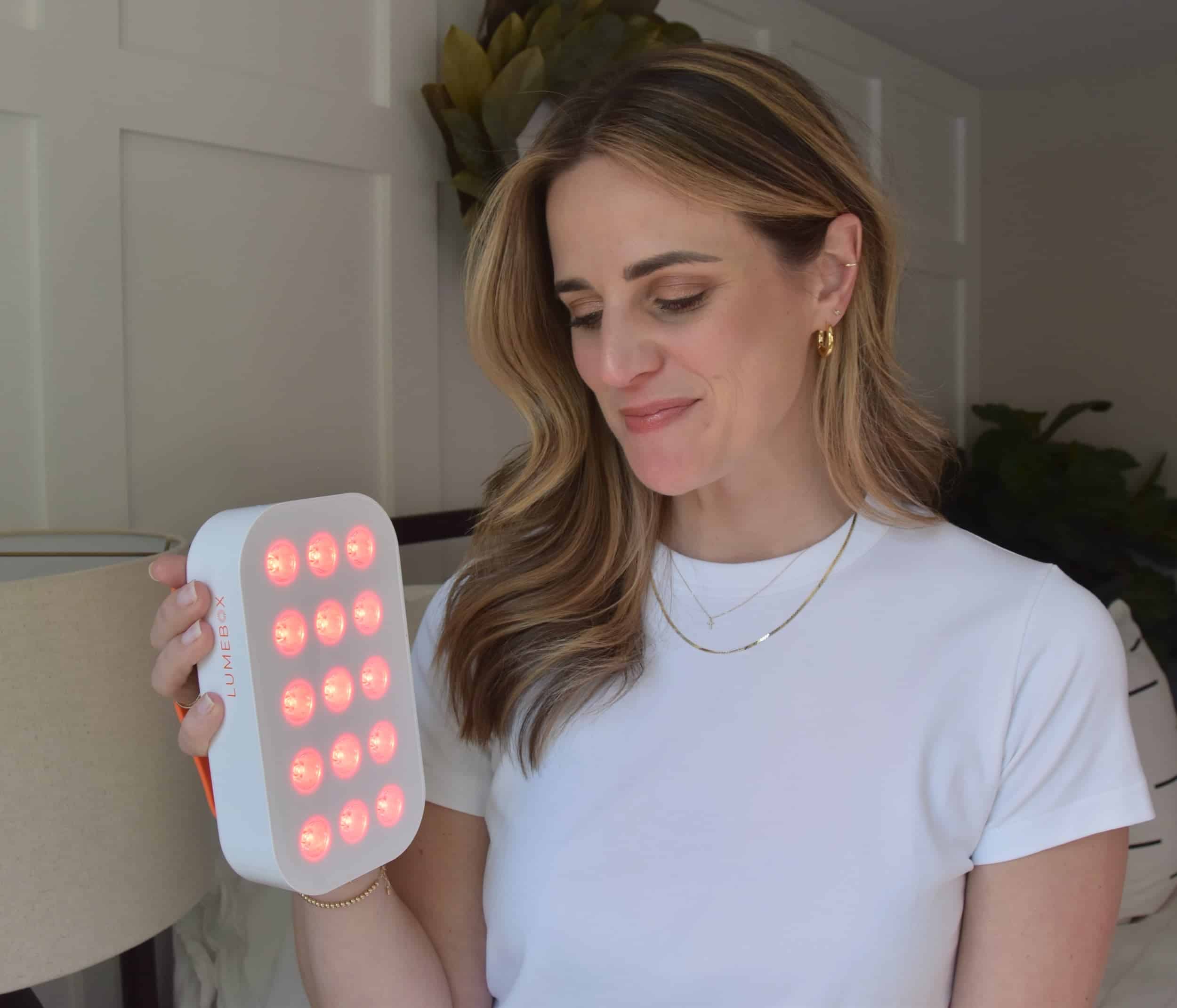 Noelle holding a lumebox red light therapy device looking down to review the settings with it on shinning on her.