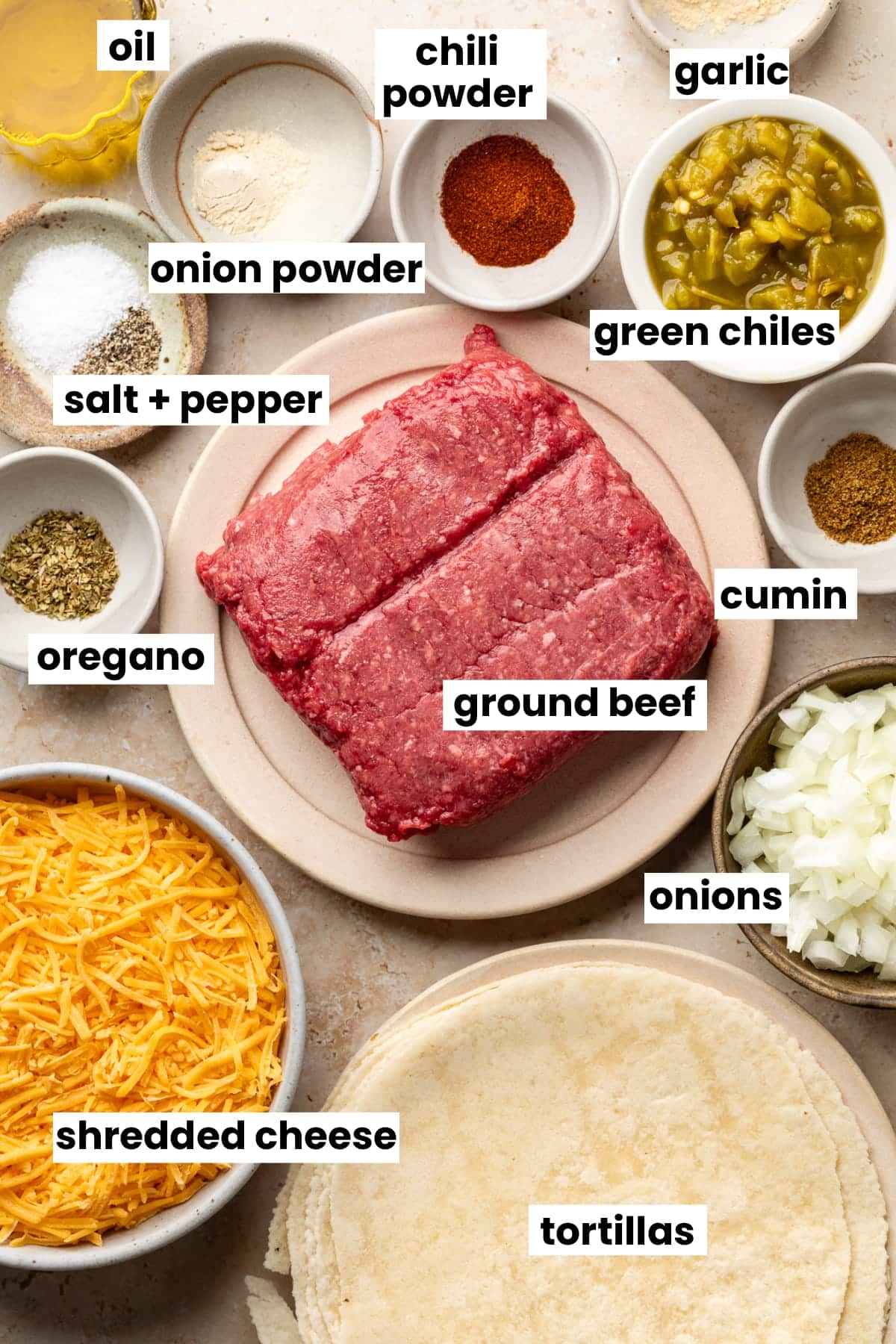Ingredients in the tacos, including ground meat, onions, tortillas, shredded cheese, oregano, green chiles, cumin, onion powder, chili powder, garlic, oil, salt, and pepper.