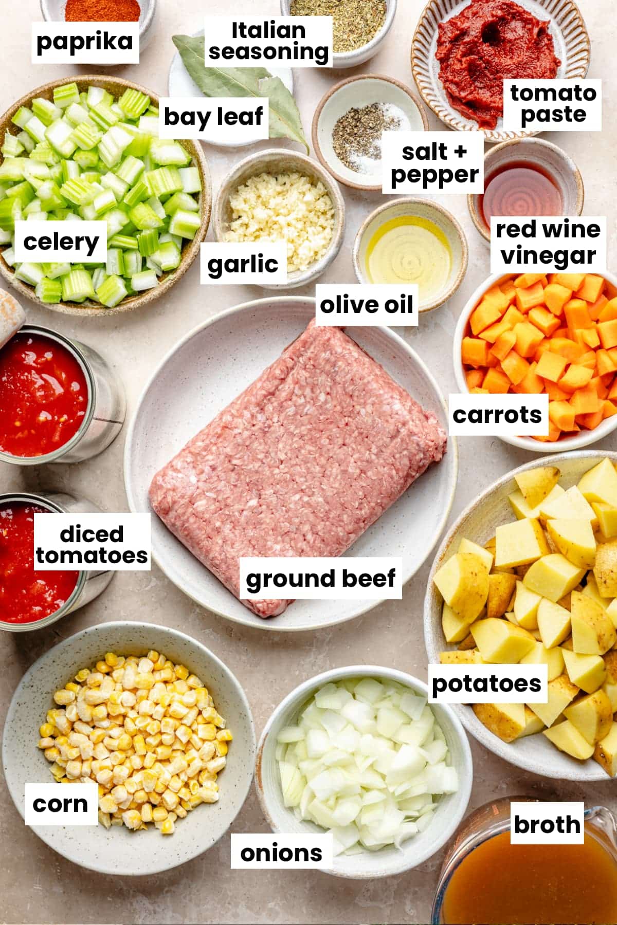 Ingredients in the recipe sectioned out into small bowls, including ground beef, celery, carrots, potatoes, tomato paste, diced tomatoes, bay leaf, paprika, cumin, salt, pepper, olive oil, red wine vinegar, onions, and broth.