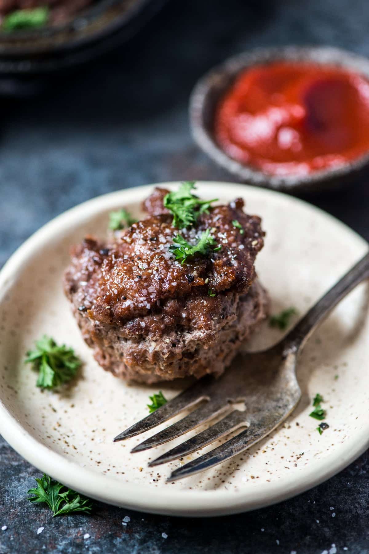 A plate with a meatloaf on it and a fork. Ketchup is served beside it for dipping.