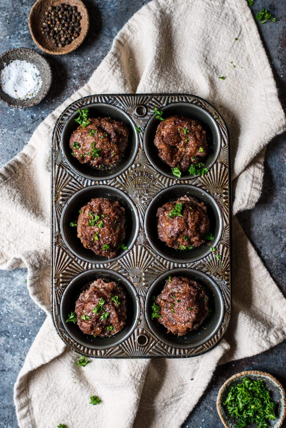 A muffin tin surrounded by ingredients for the recipe, including ground beef, salt, pepper, ketchup, and cream of tartar.