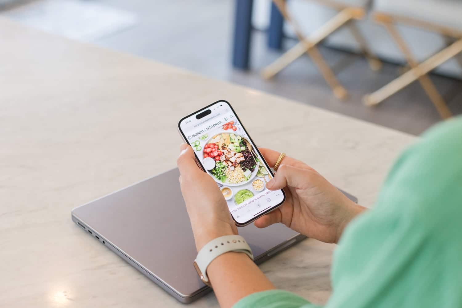 A woman sitting at the table reviewing healthy nutrition info and a recipe on her phone.