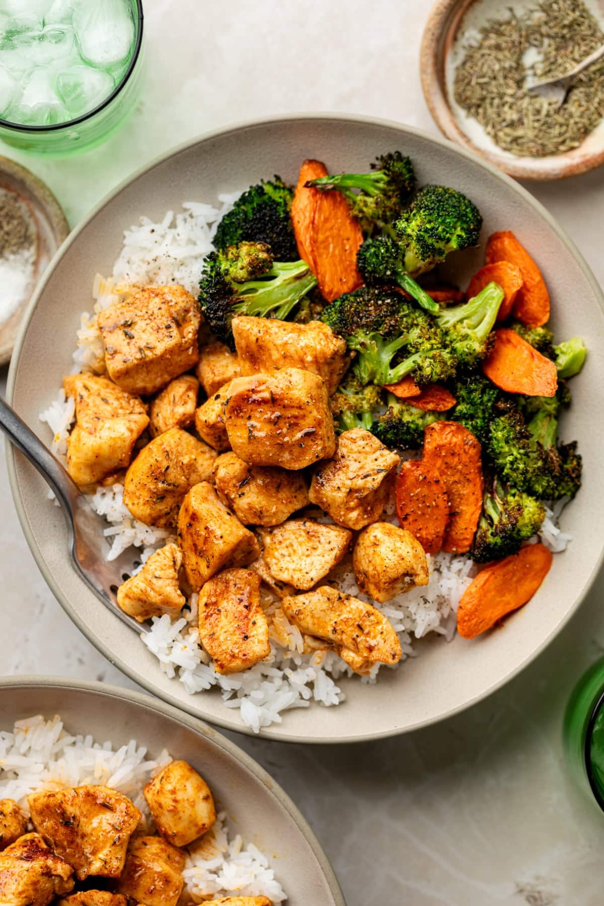 A tan plate with rice, vegetables, and chicken bites with a fork on a table ready to eat.