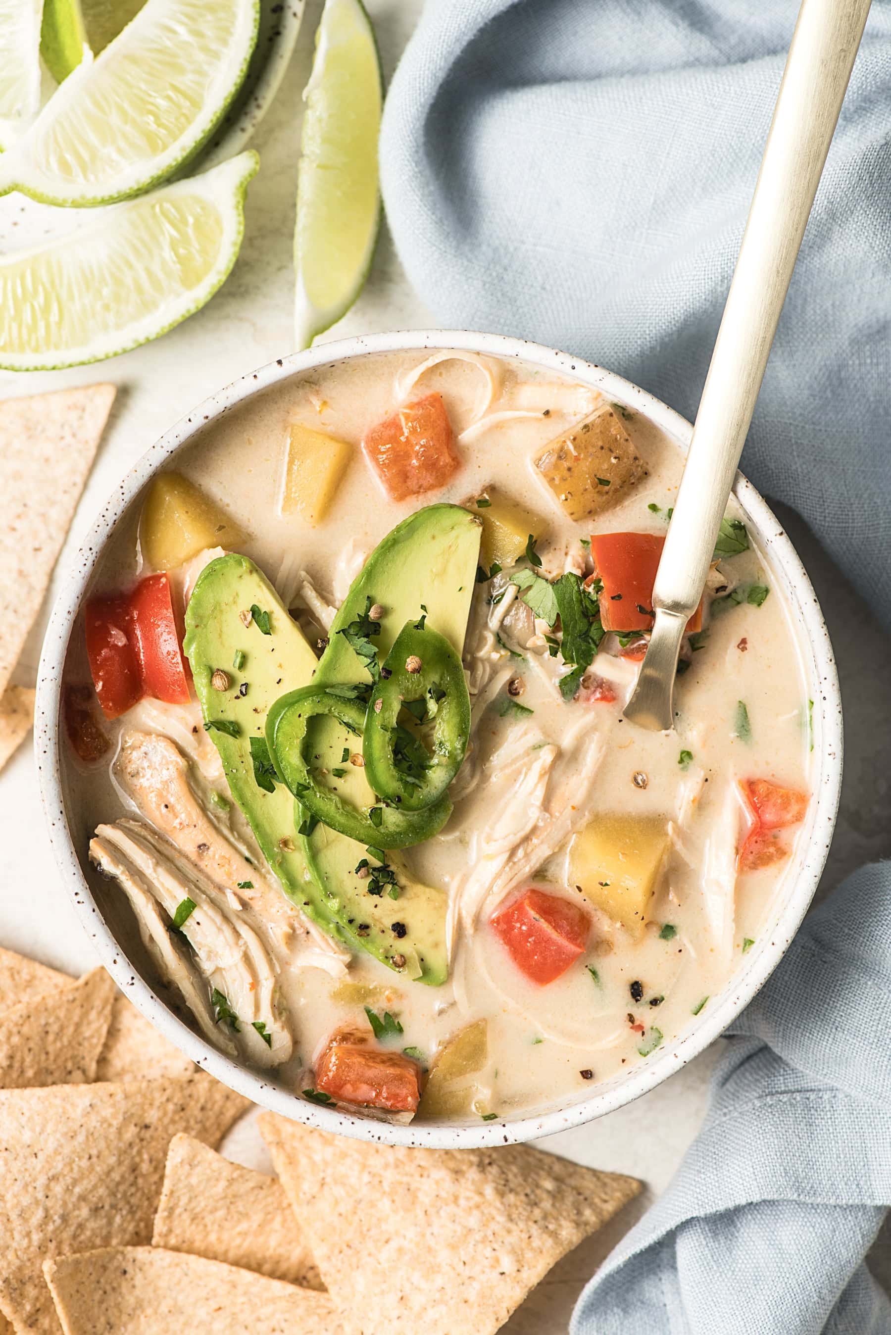 A large bowl of the white chicken chili with a spoon and a napkin.