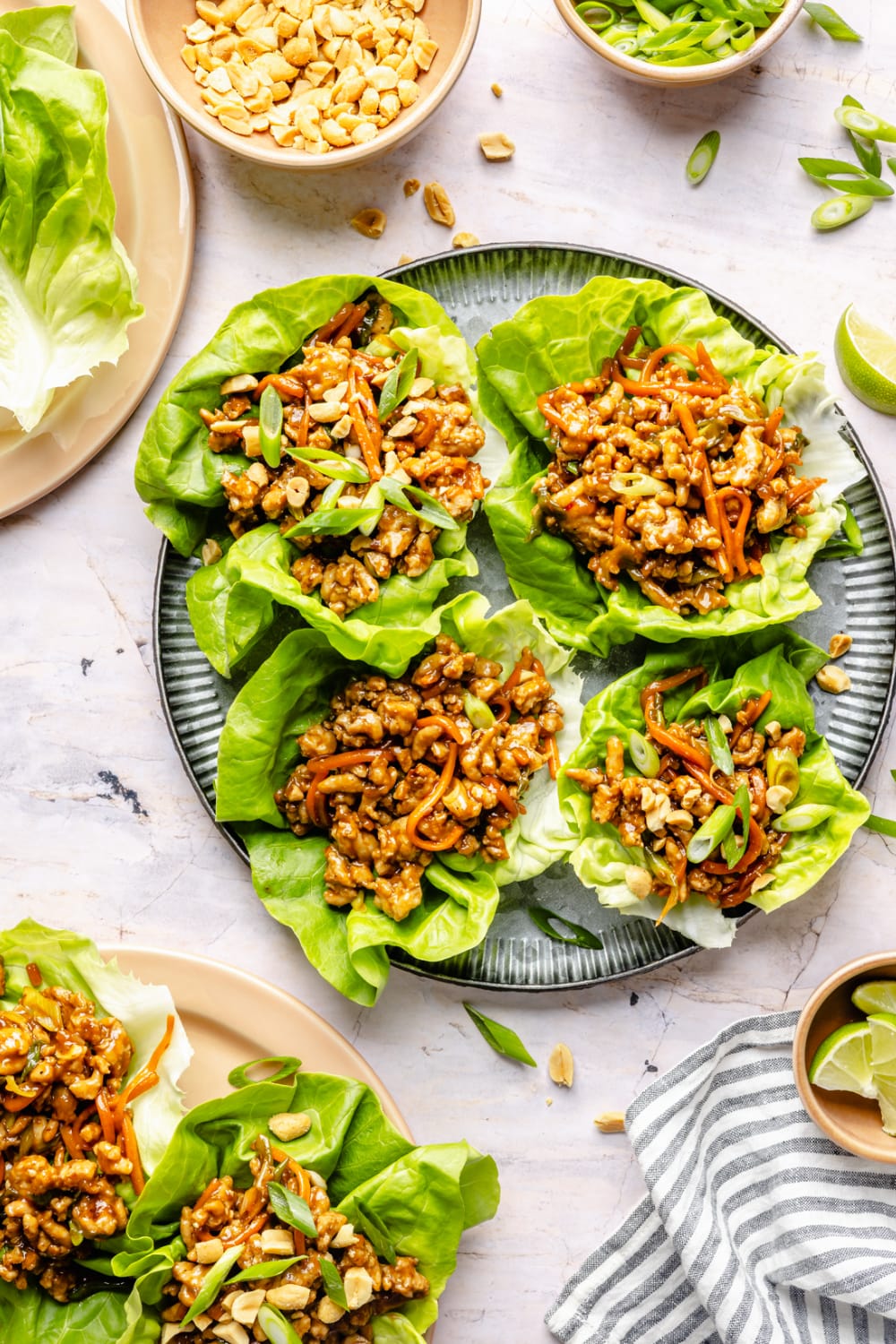 A table with a large plate with Thai chicken lettuce wraps already assembled for serving, plus plates around the table with lettuce wraps already being eaten.