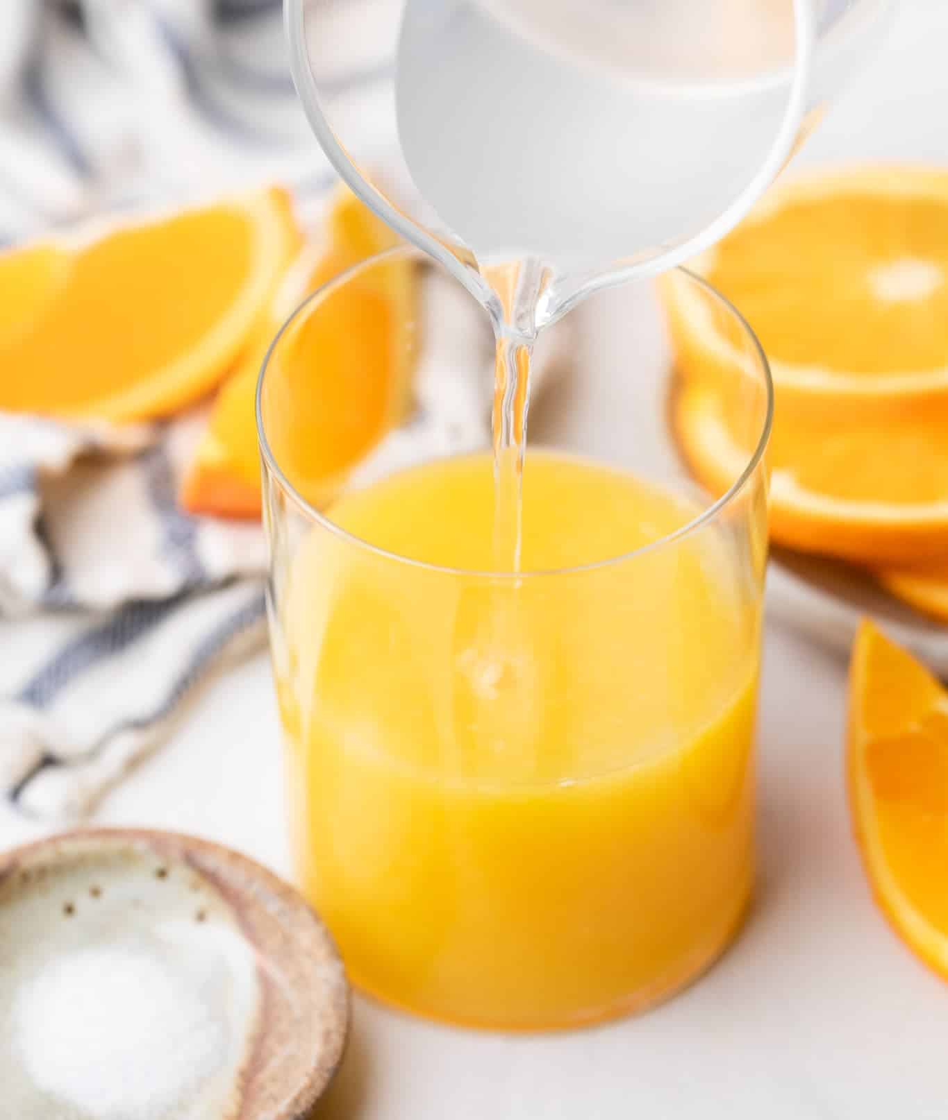 Adding coconut water and orange juice together in a small glass.