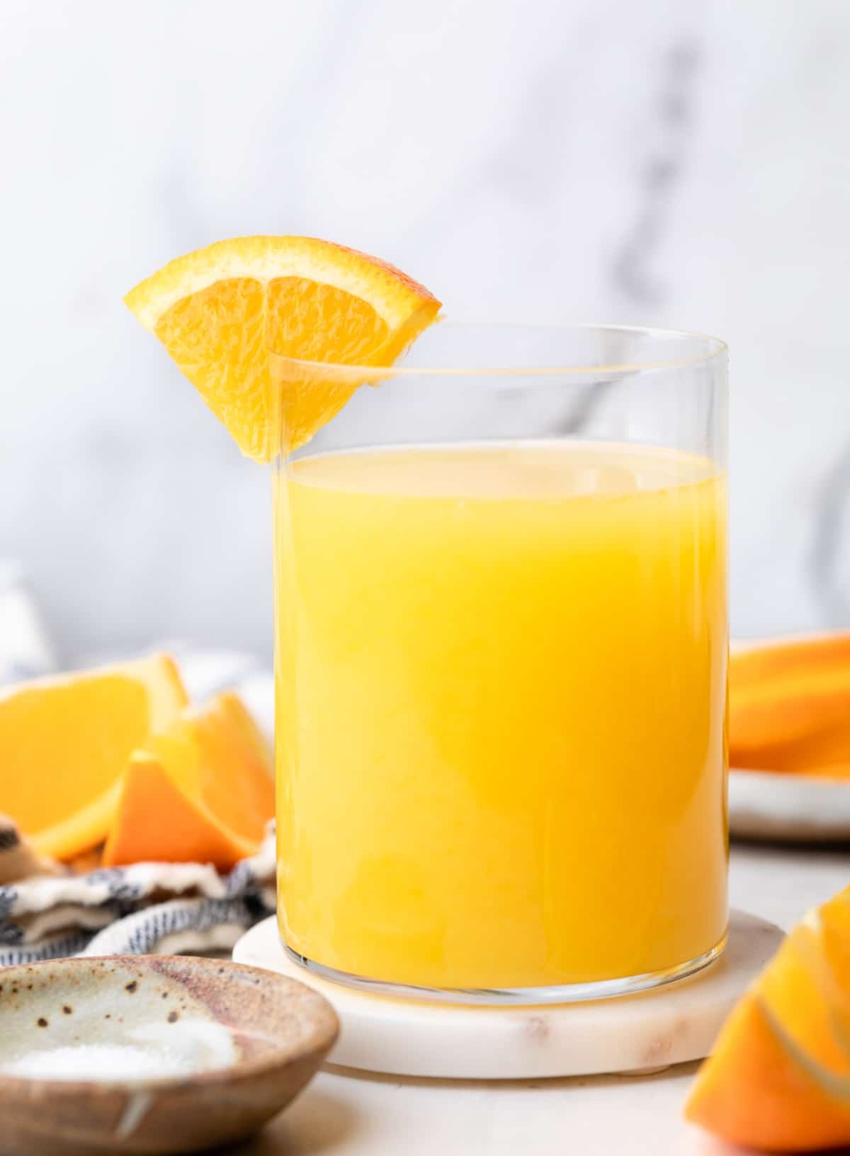 A small glass of an adrenal cocktail and a slice of orange on the glass.