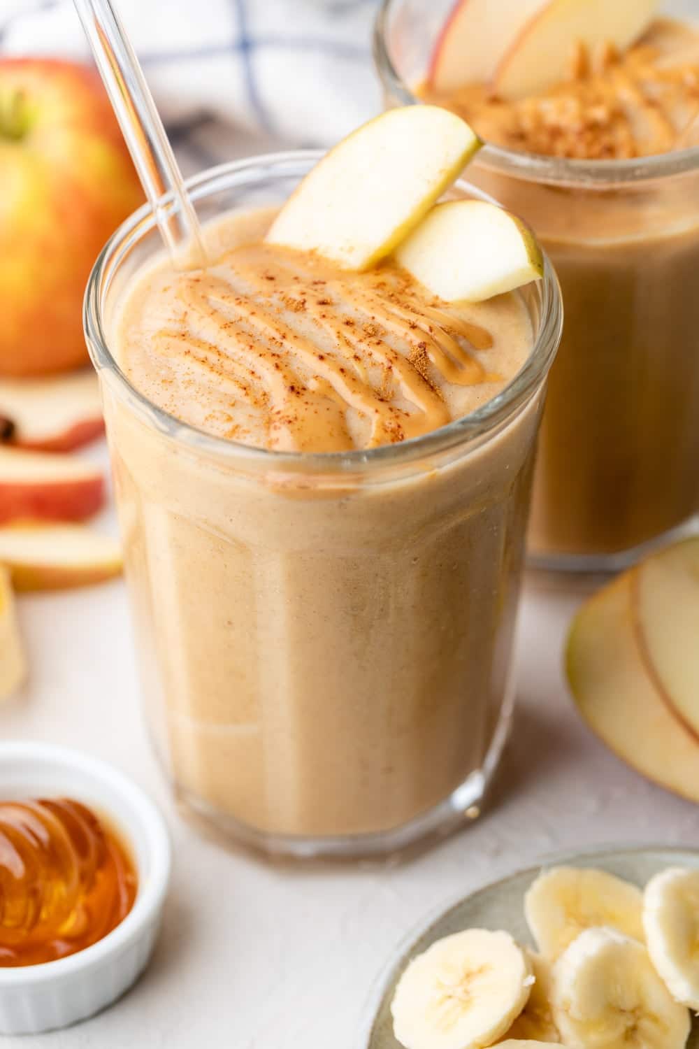 A tall smoothie with apples, bananas, and a drizzle of caramel sauce on top.