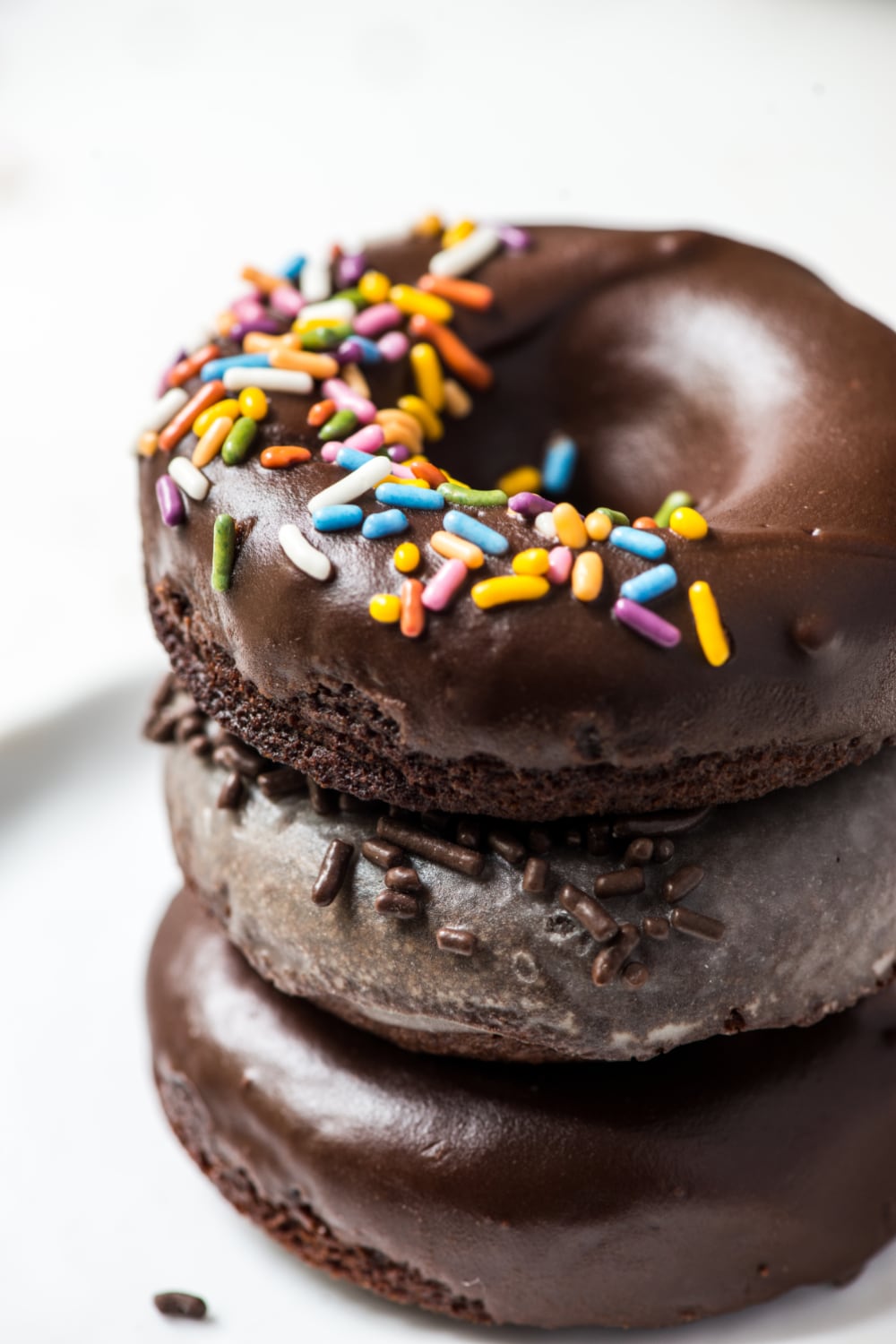 a stack of three baked donuts with glaze and chocolate frosting