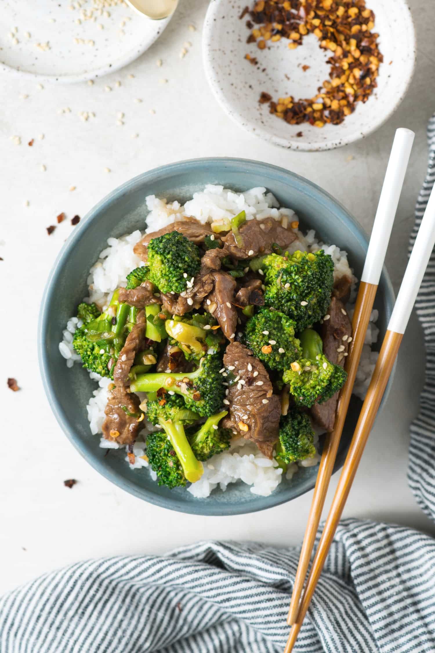 A bowl of rice with beef and broccoli on top with utensils. 