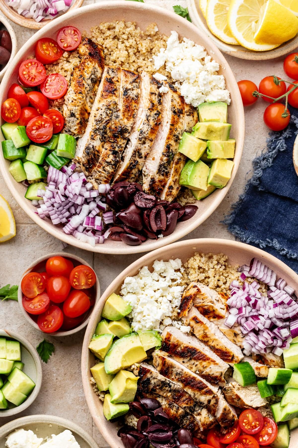 Two bowls on the table fully prepared and ready to eat, surrounded by tomatoes, lemon, and other Mediterranean flavors.