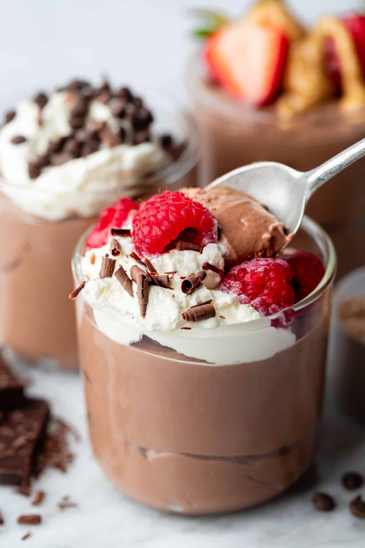 A spoon dipped into the chocolate pudding with berries and cream on top.