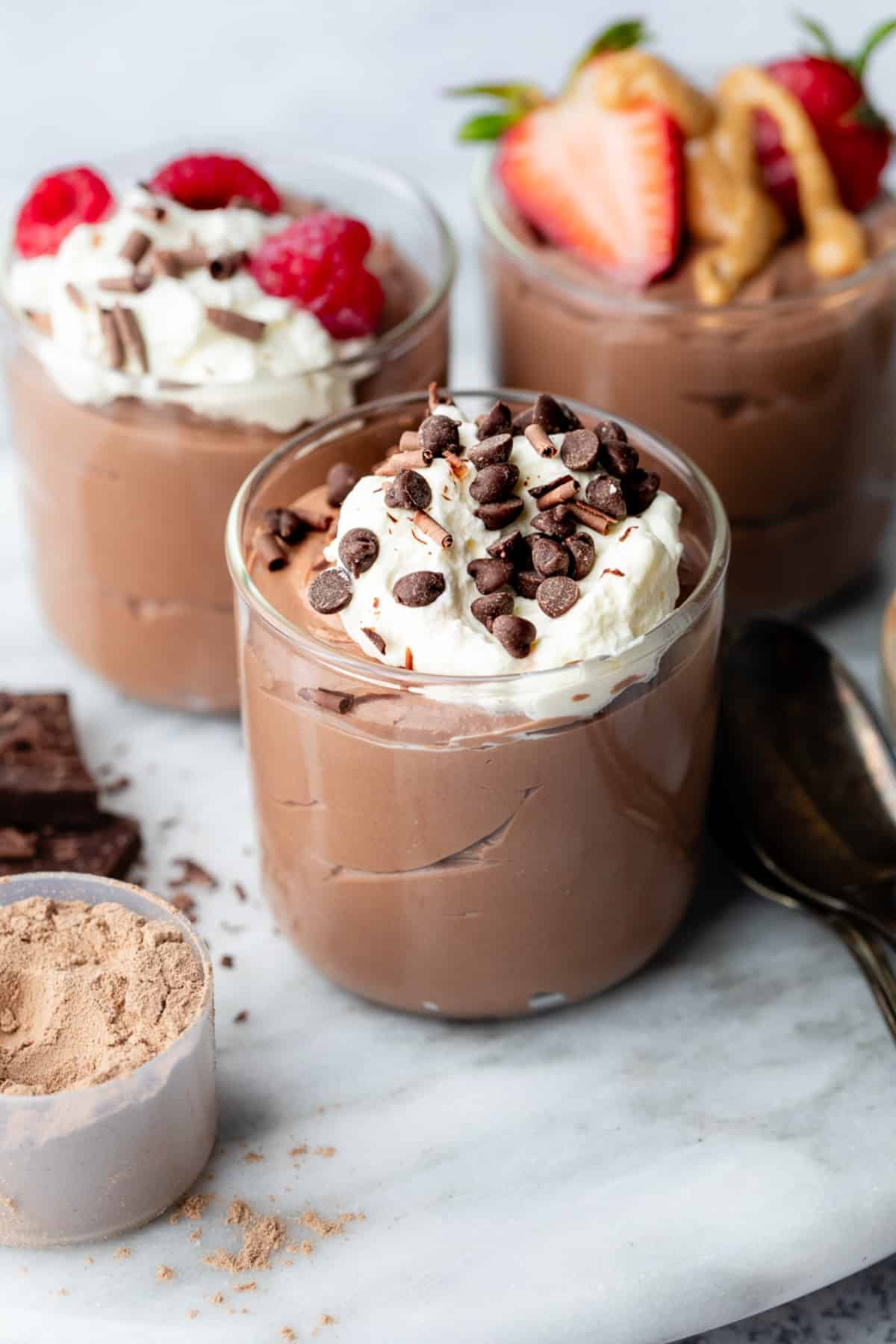 A clear jar with thick and creamy chocolate protein pudding topped with whipped cream and chocolate chips.