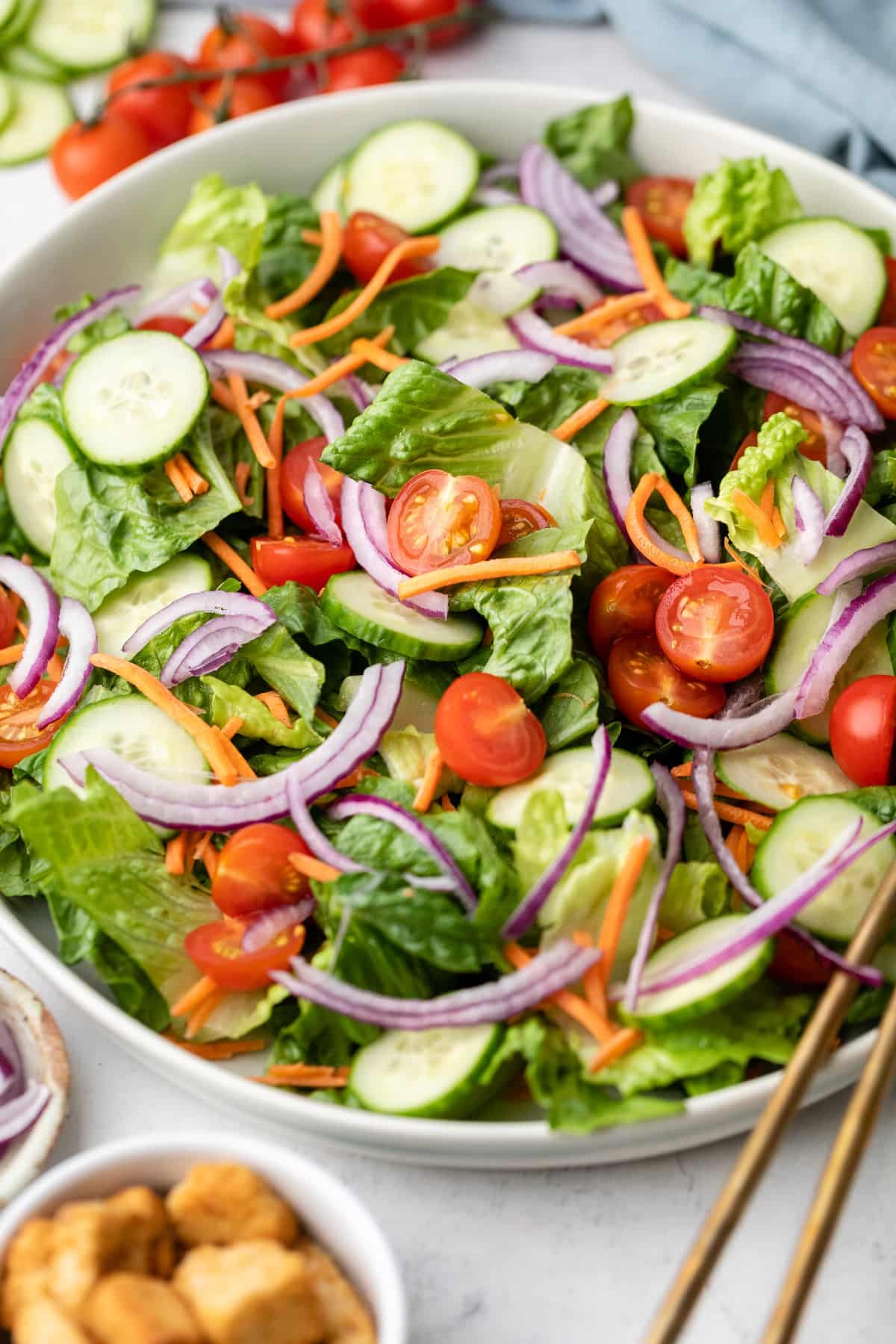 Close up of tomatoes, red onion, green lettuce, cucumbers, and carrots in a large salad bowl.