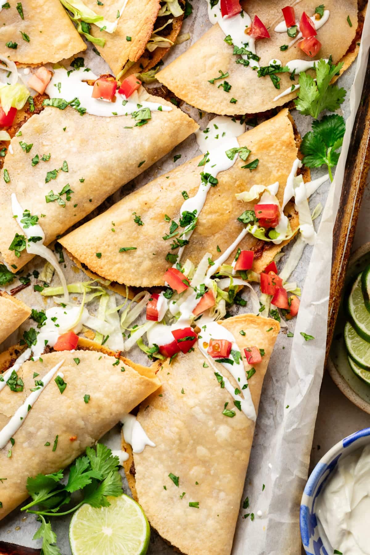 A handful of tacos on the pan covered in optional toppings, including sour cream, cilantro, and diced tomato.
