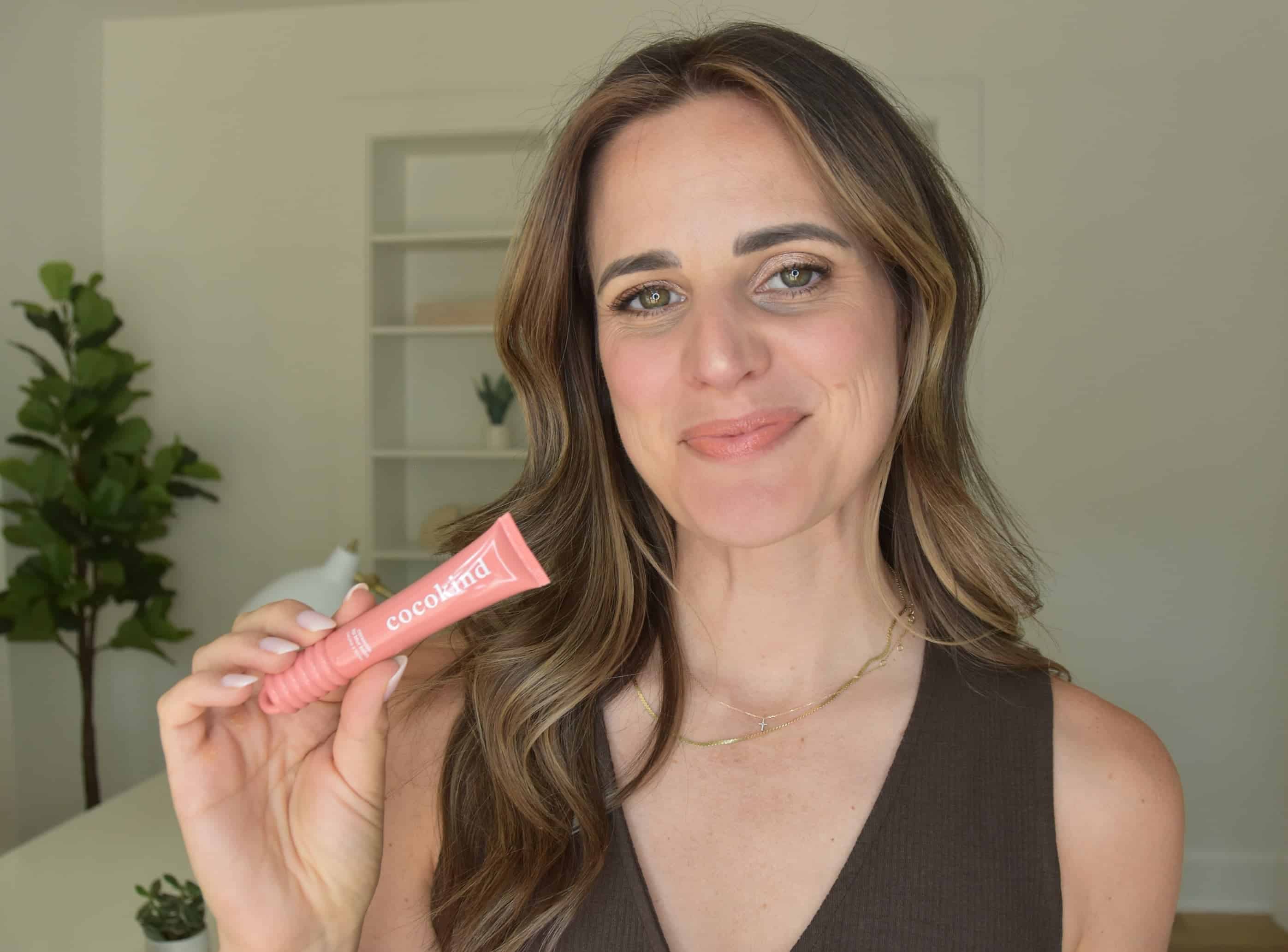 Noelle holding a cocokind lip balm and wearing the color on her lips for review.