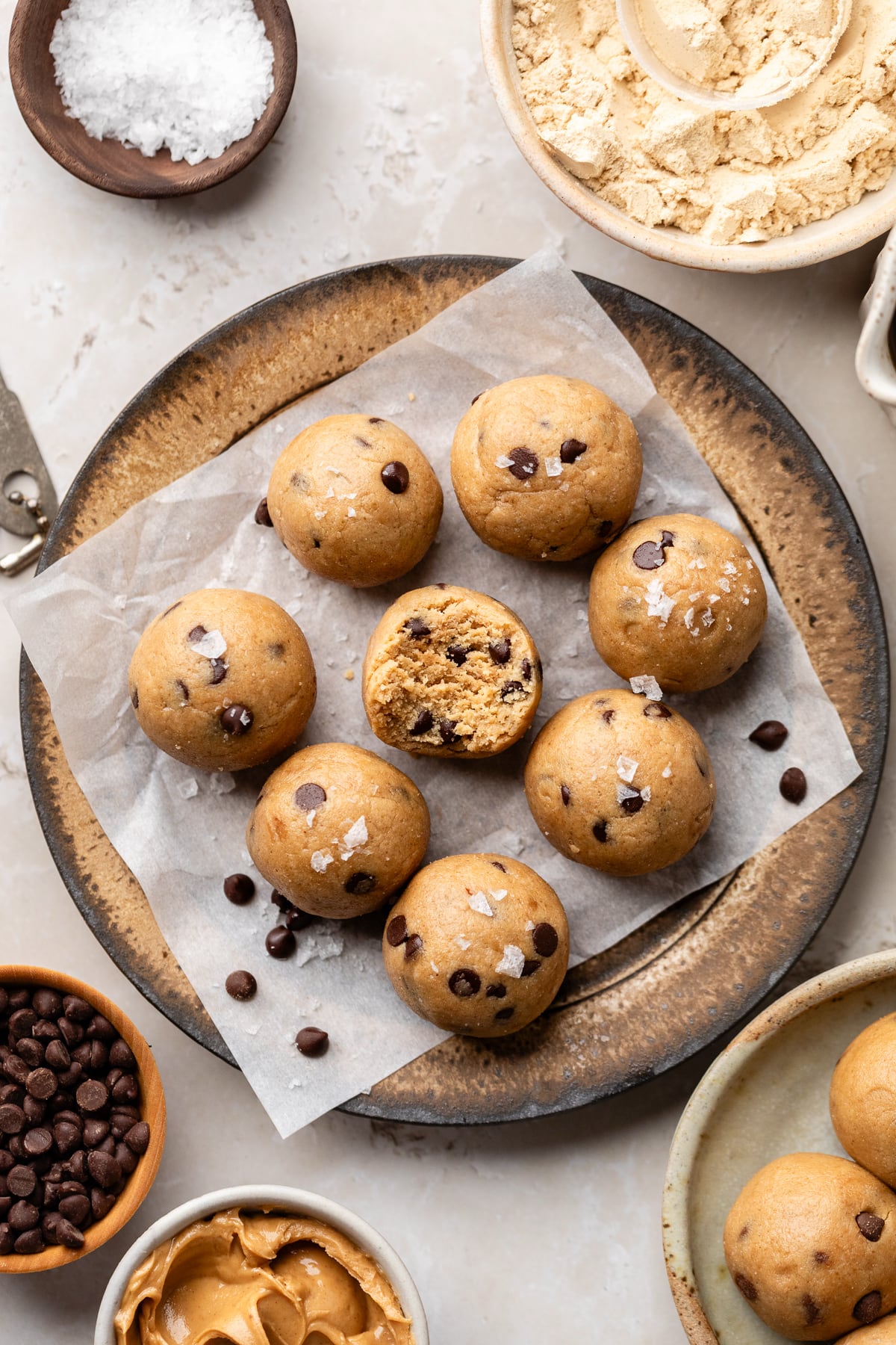 A plate with parchment paper and eight cookie dough protein balls with one that has a bite taken out.