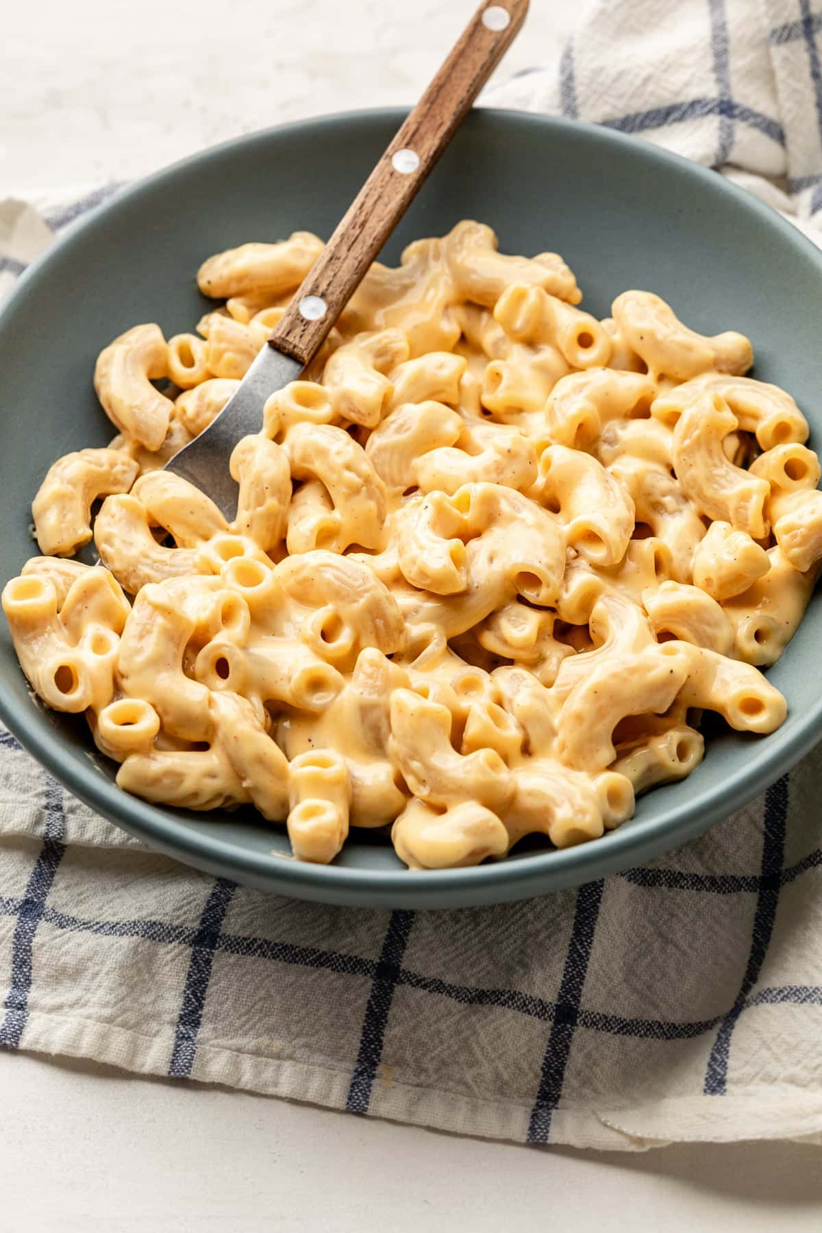 A bowl with a serving of macaroni and cheese and a spoon on a napkin.