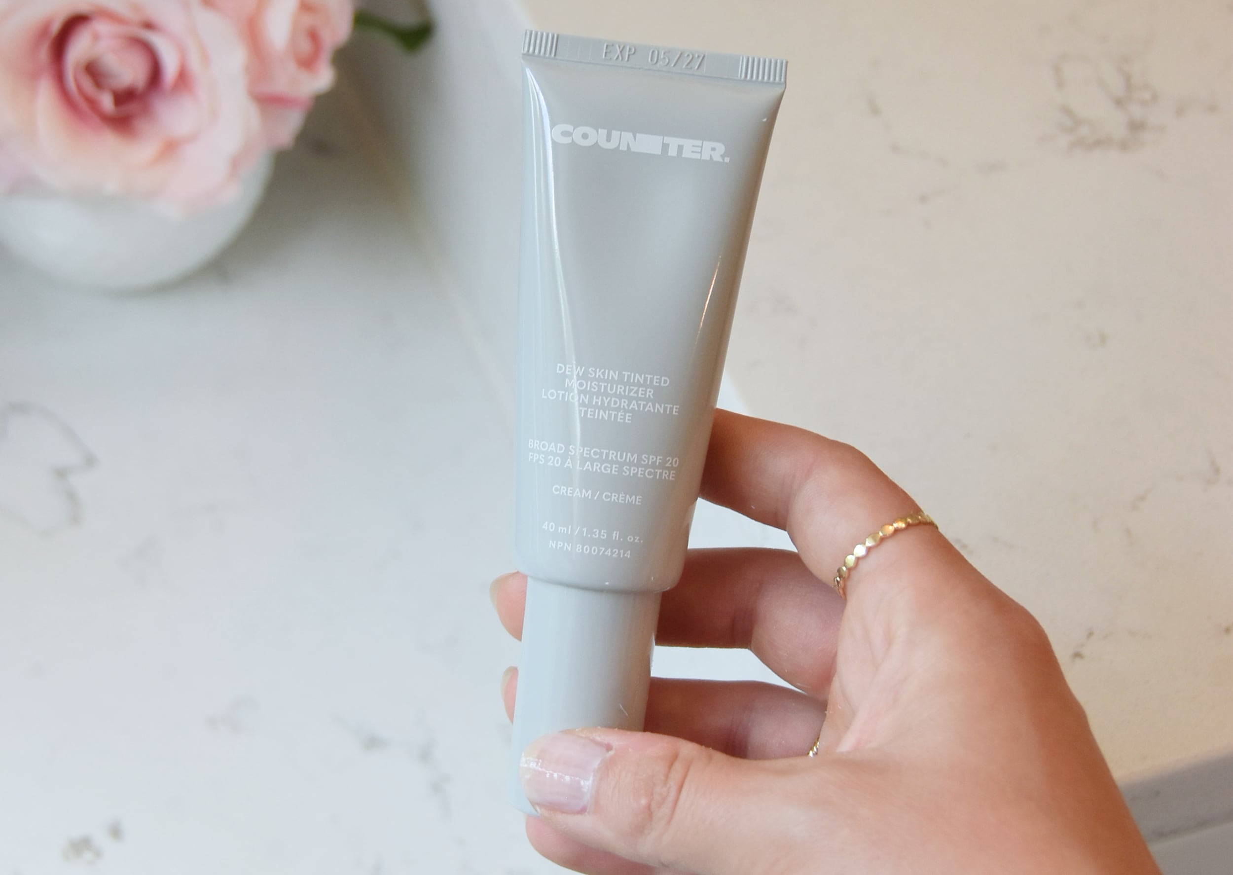 Holding the newly packaged Dew Skin Tinted Moisturizer in the bathroom over a makeup counter.