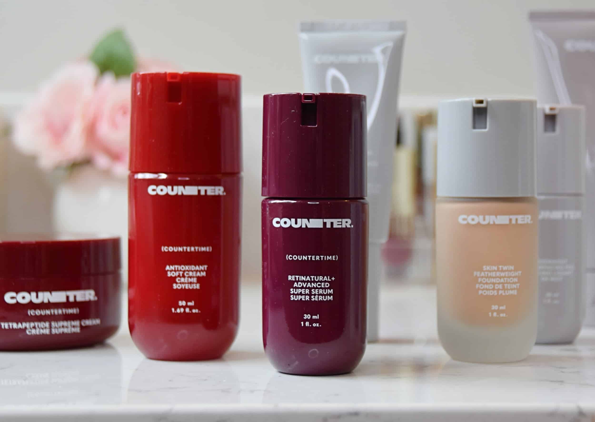 A handful of Counter skin care products on the counter in front of a vase with roses.