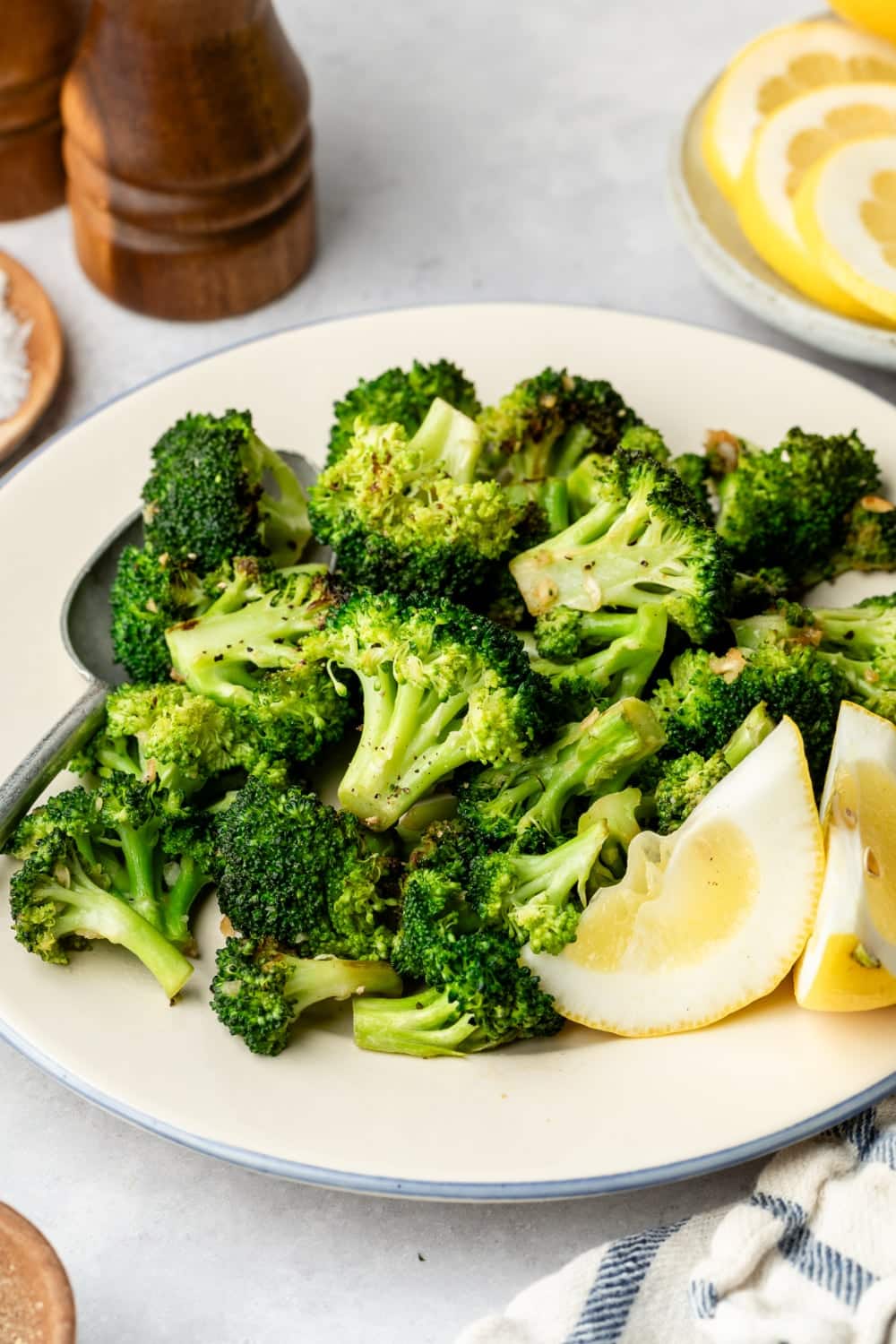 A plate laying on the table with the finished dish on the table surrounded by lemon wedges, a serving spoon, and salt and pepper.