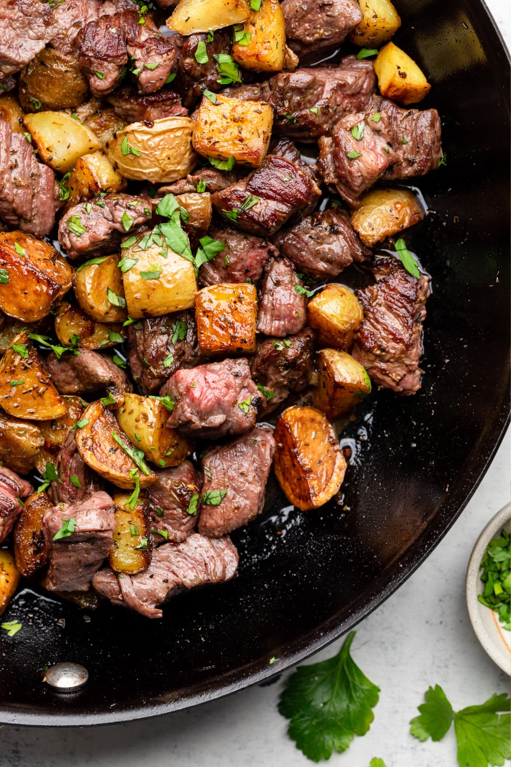 Steak bites and potatoes finished in a skillet with parsley on top.