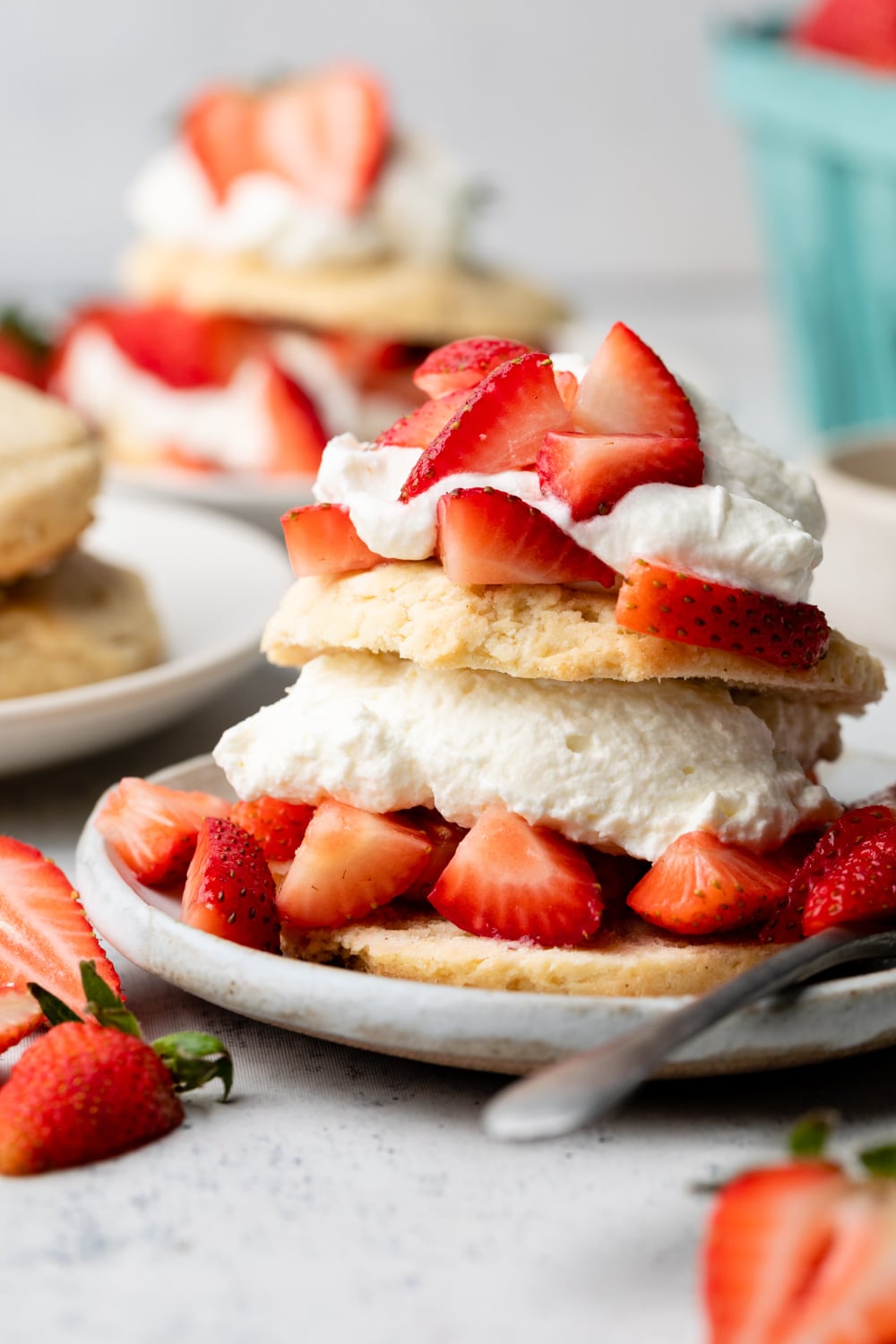 Plate with layers of gluten free shortcake biscuits, whipped cream, and strawberries with a fork on the side.