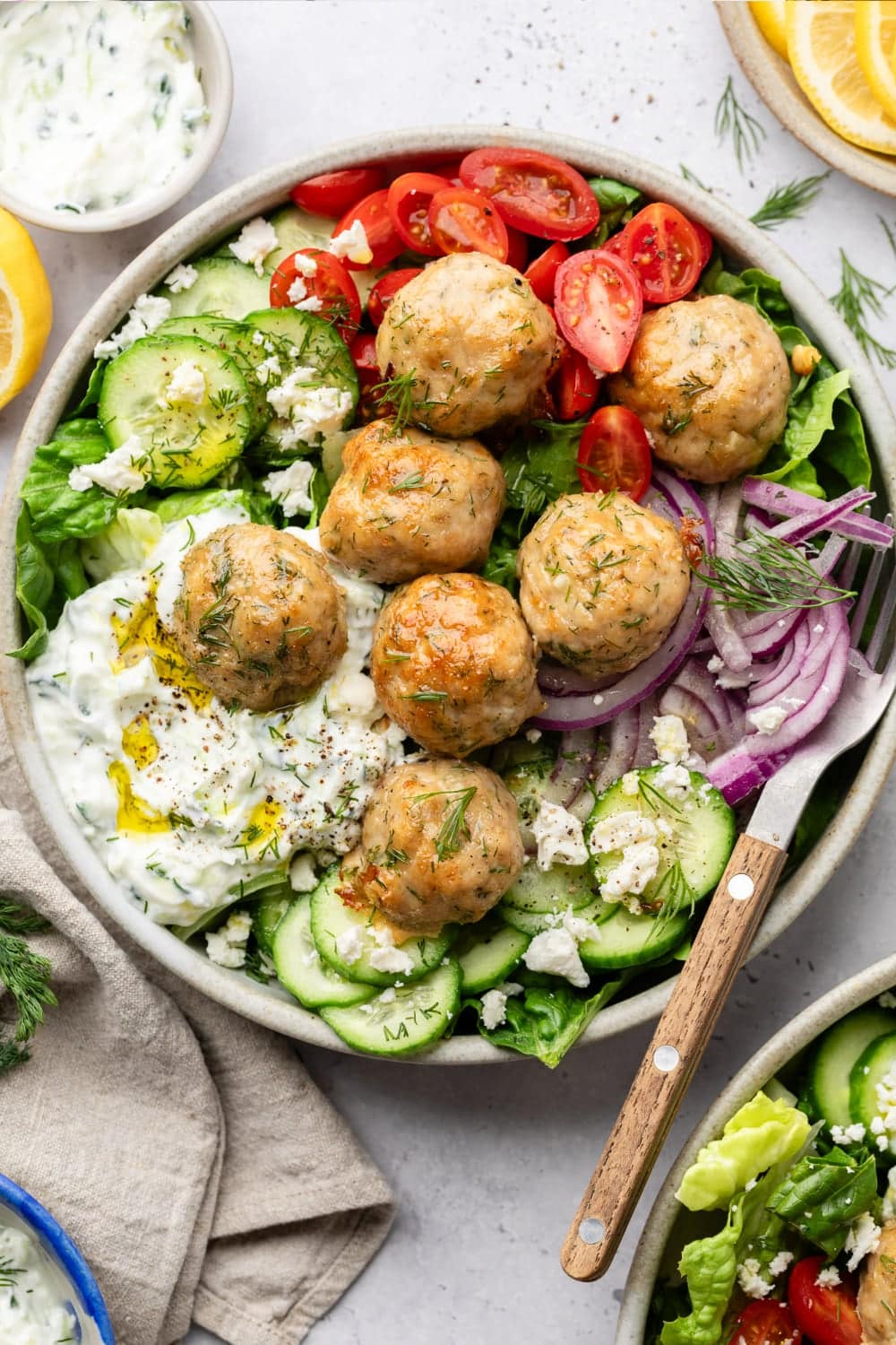 A Greek salad bowl topped with chicken meatballs, feta cheese, and Tzatziki sauce.