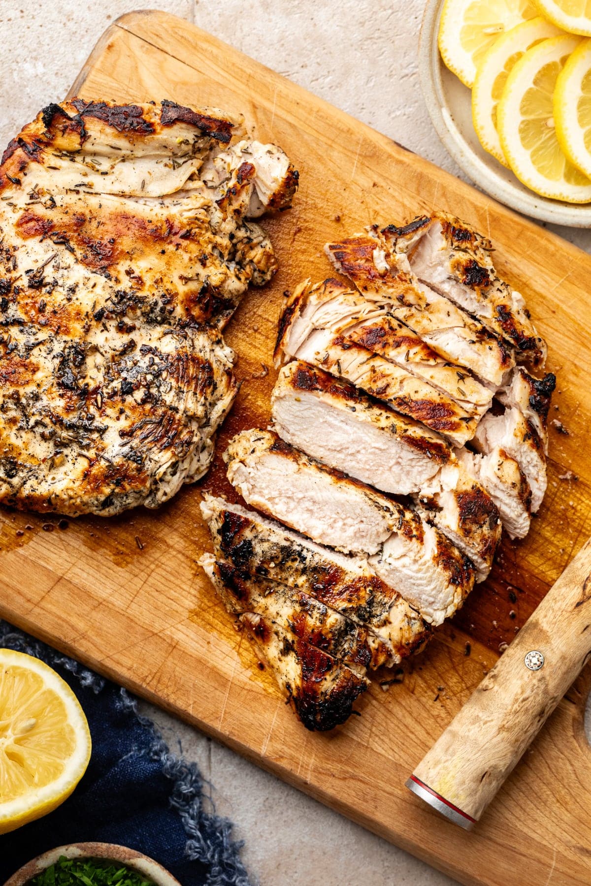 Two pieces of Greek chicken grilled and sliced on a cutting board.