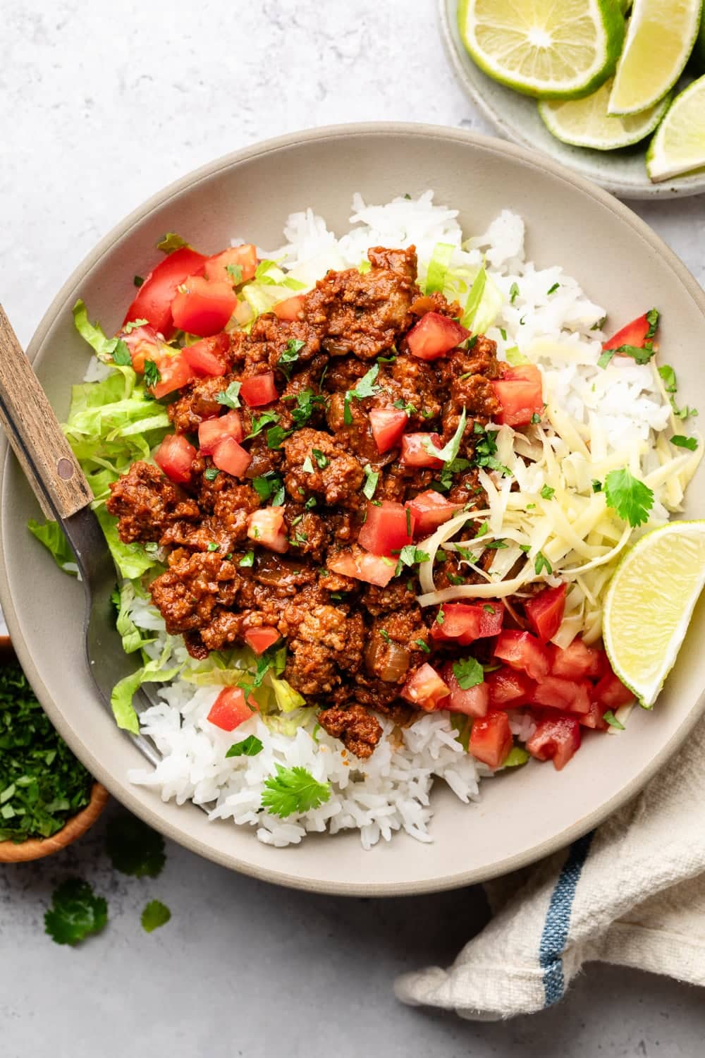 A plate of rice with shredded lettuce, tomatoes, lime wedges, and the taco meat on top.