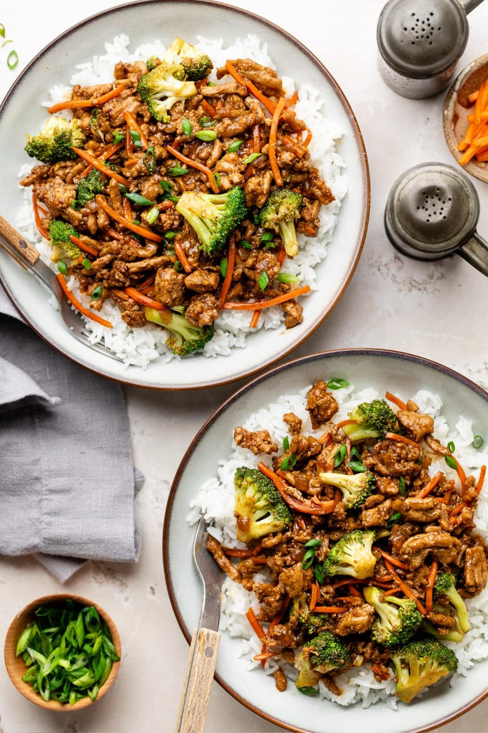 Two bowls of ground turkey teriyaki served on a table with napkins and two forks for eating.