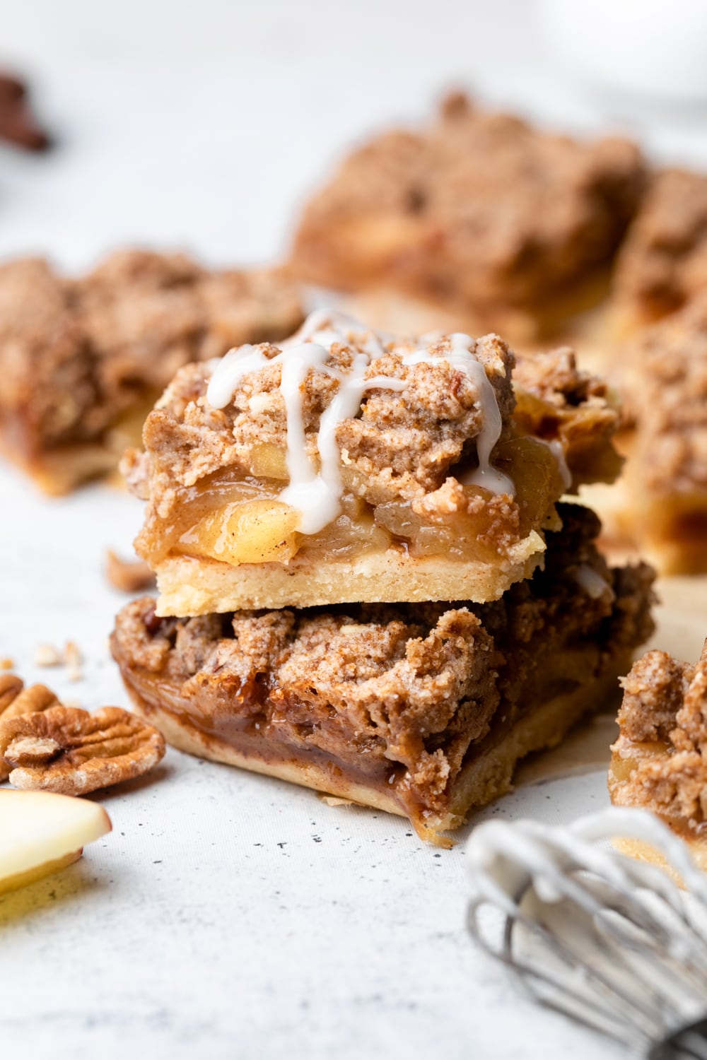 Two apple pie bars made with healthier ingredients stacked with a drizzle of glaze.