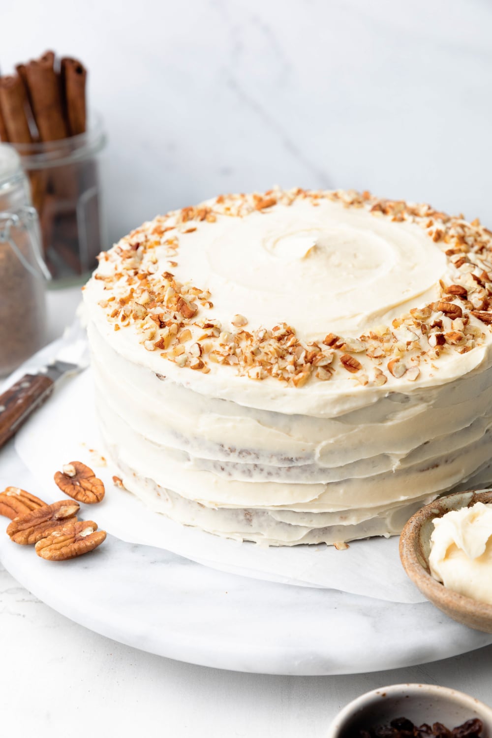 whole healthy carrot cake decorated with frosting and pecans.
