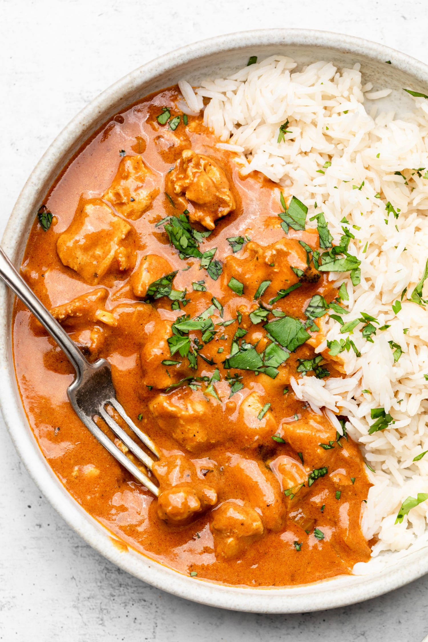 A bowl of healthy chicken tikka masala with rice and a fork.