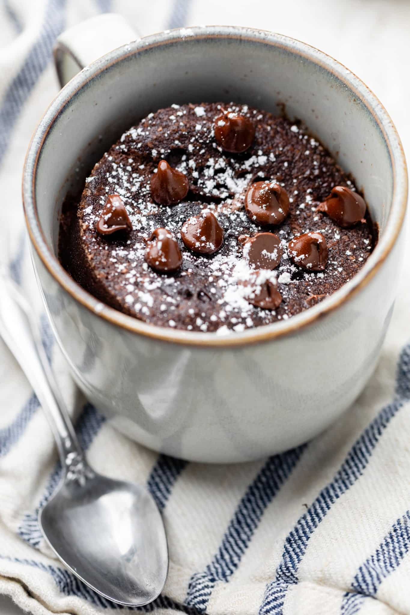 A mug with the cake baked inside with chocolate chips and powdered sugar on top.