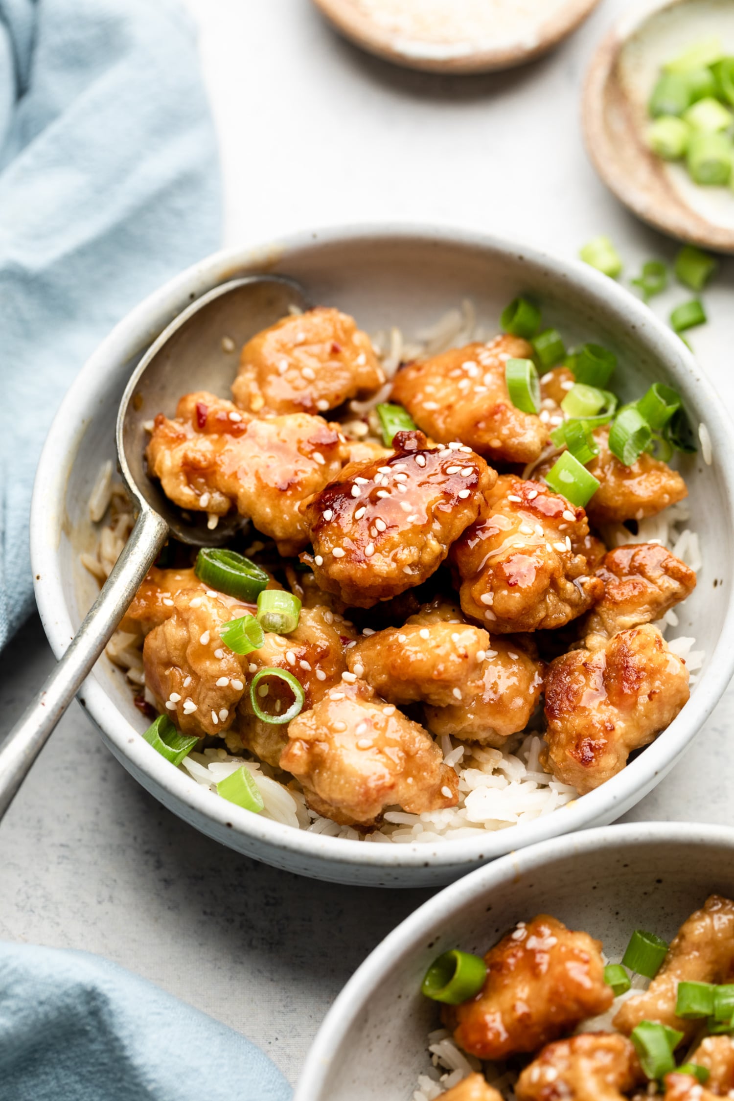 A bowl of healthy orange chicken after it's been baked in the oven served in a bowl with a spoon.