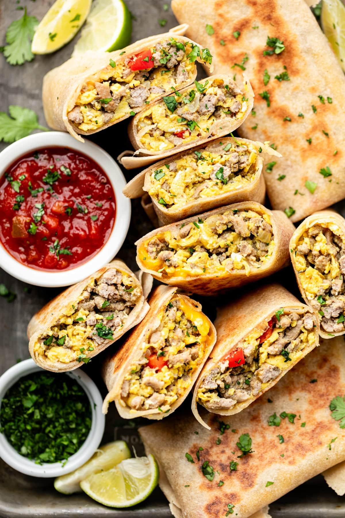 A tray of high protein breakfast burritos cut in half for serving with salsa and fresh herbs.