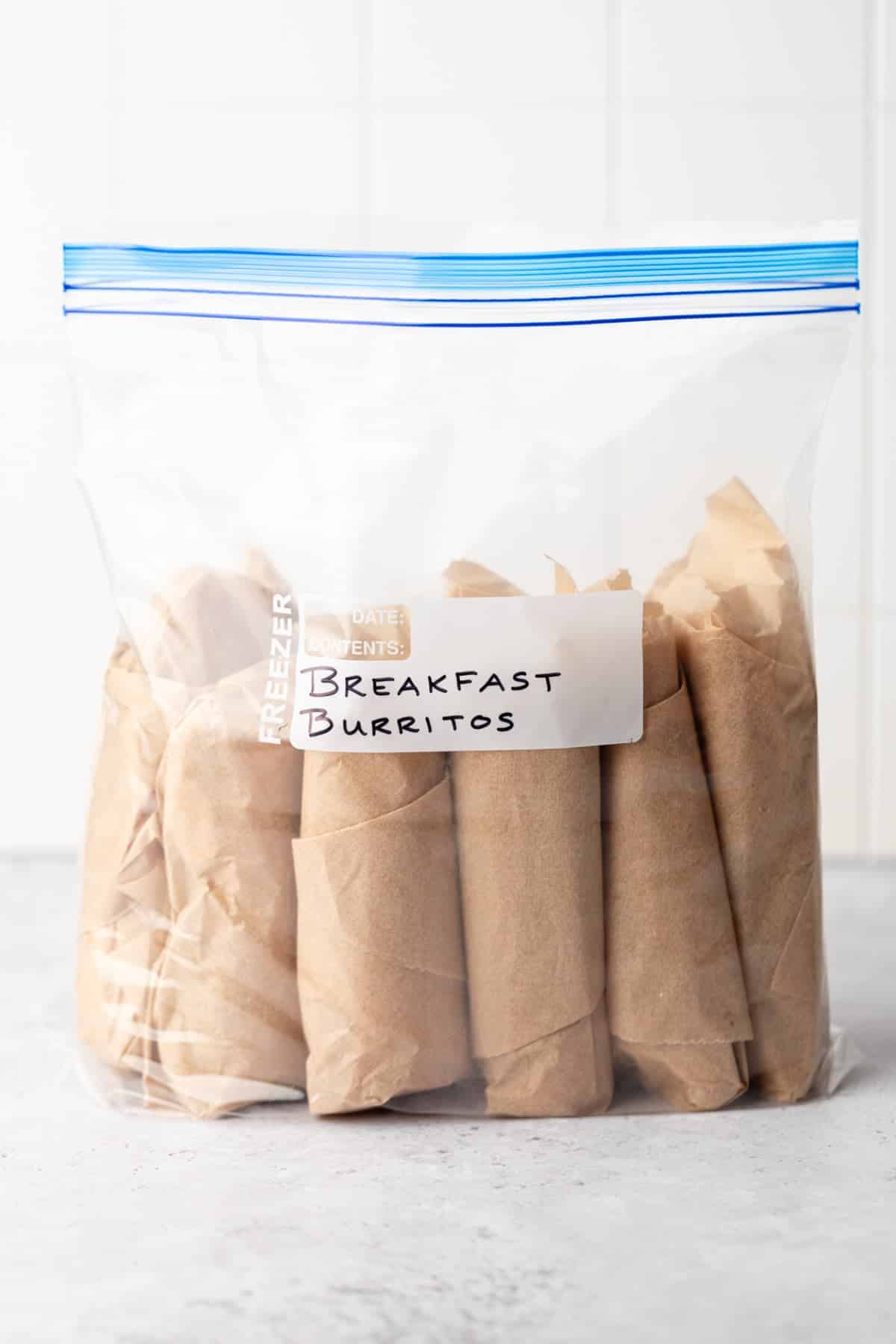 Six breakfast burritos wrapped in parchment paper in a storage bag ready to be thrown in the freezer.