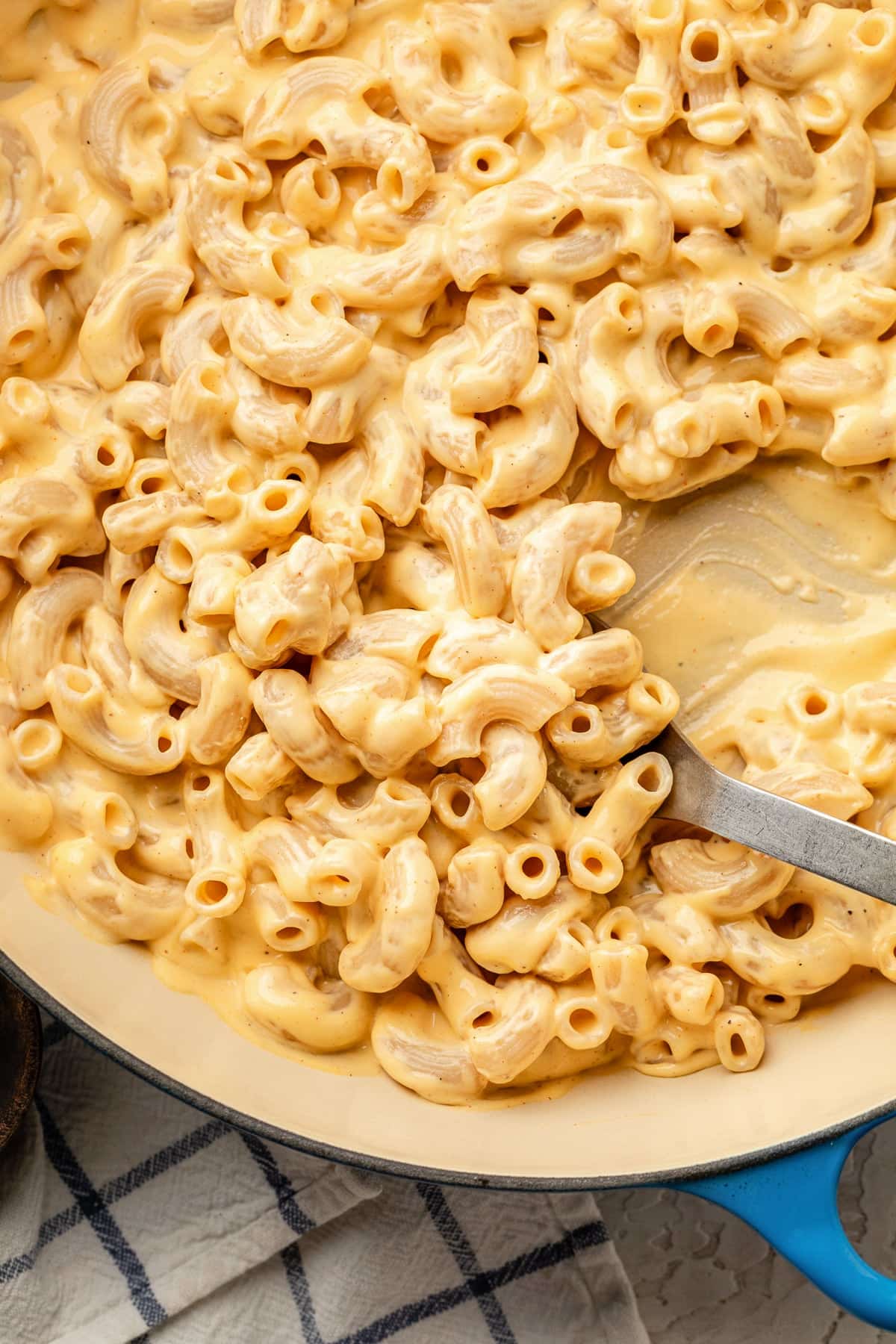 A close up of high protein mac and cheese in a skillet with a spoon for serving.