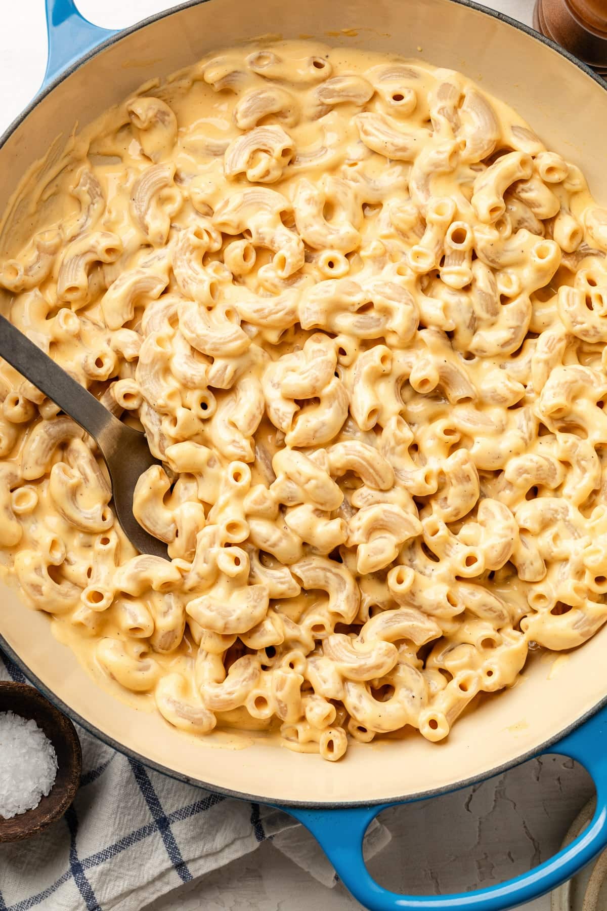 A skillet with high protein mac and cheese made with cottage cheese in a pan being stirred with a spoon.