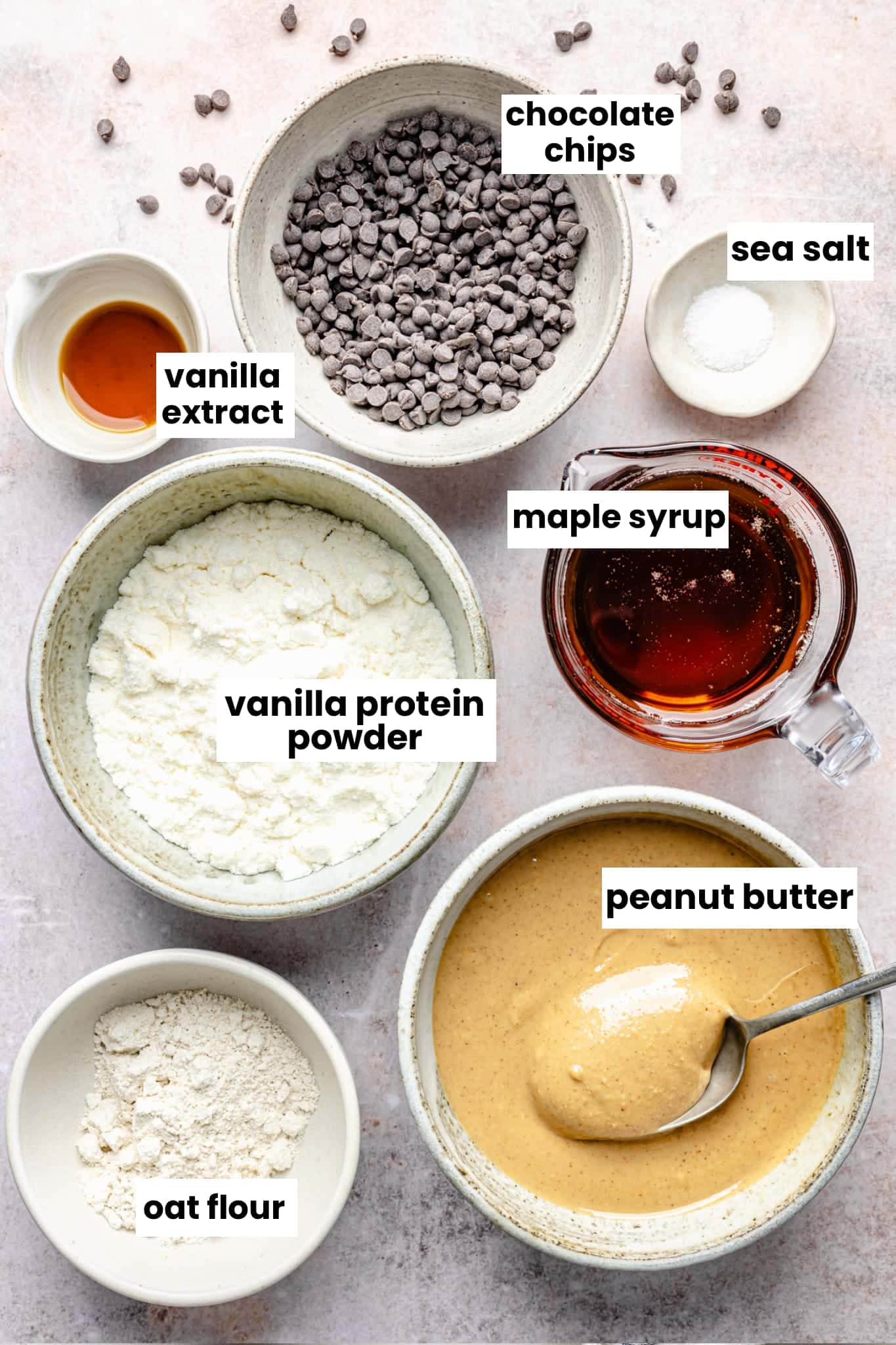 Ingredients in the recipe, including peanut butter, vanilla protein powder, maple syrup, oat flour, vanilla extract, chocolate chips, and sea salt.