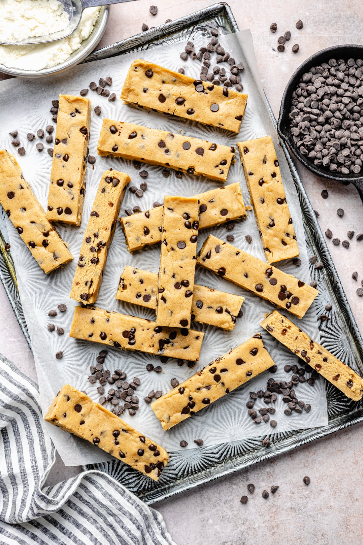 All of the cut up bars on a baking pan surrounded by chocolate chips.