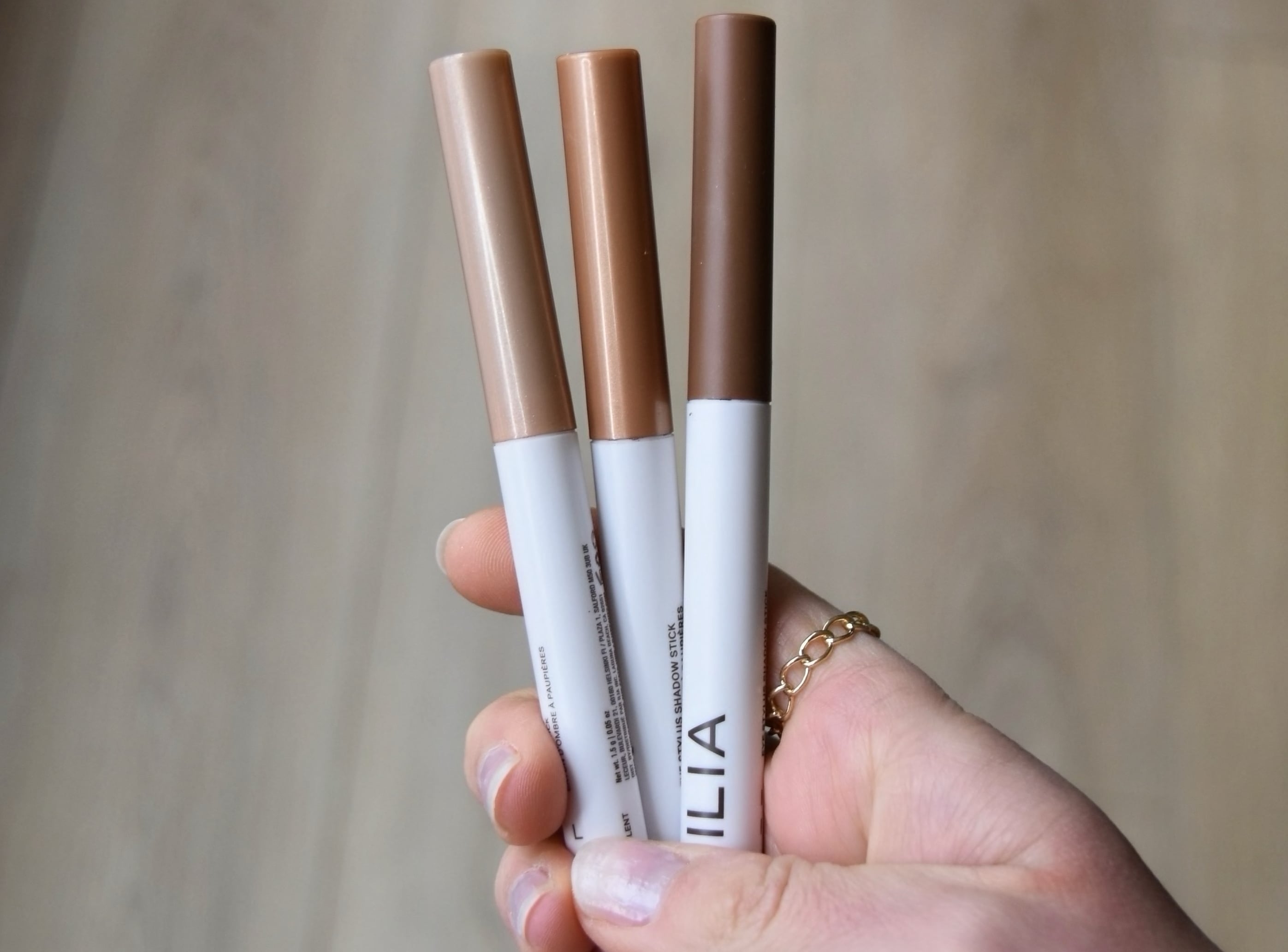 Holding three eye shadow stylus sticks, and showing the colors of each one.