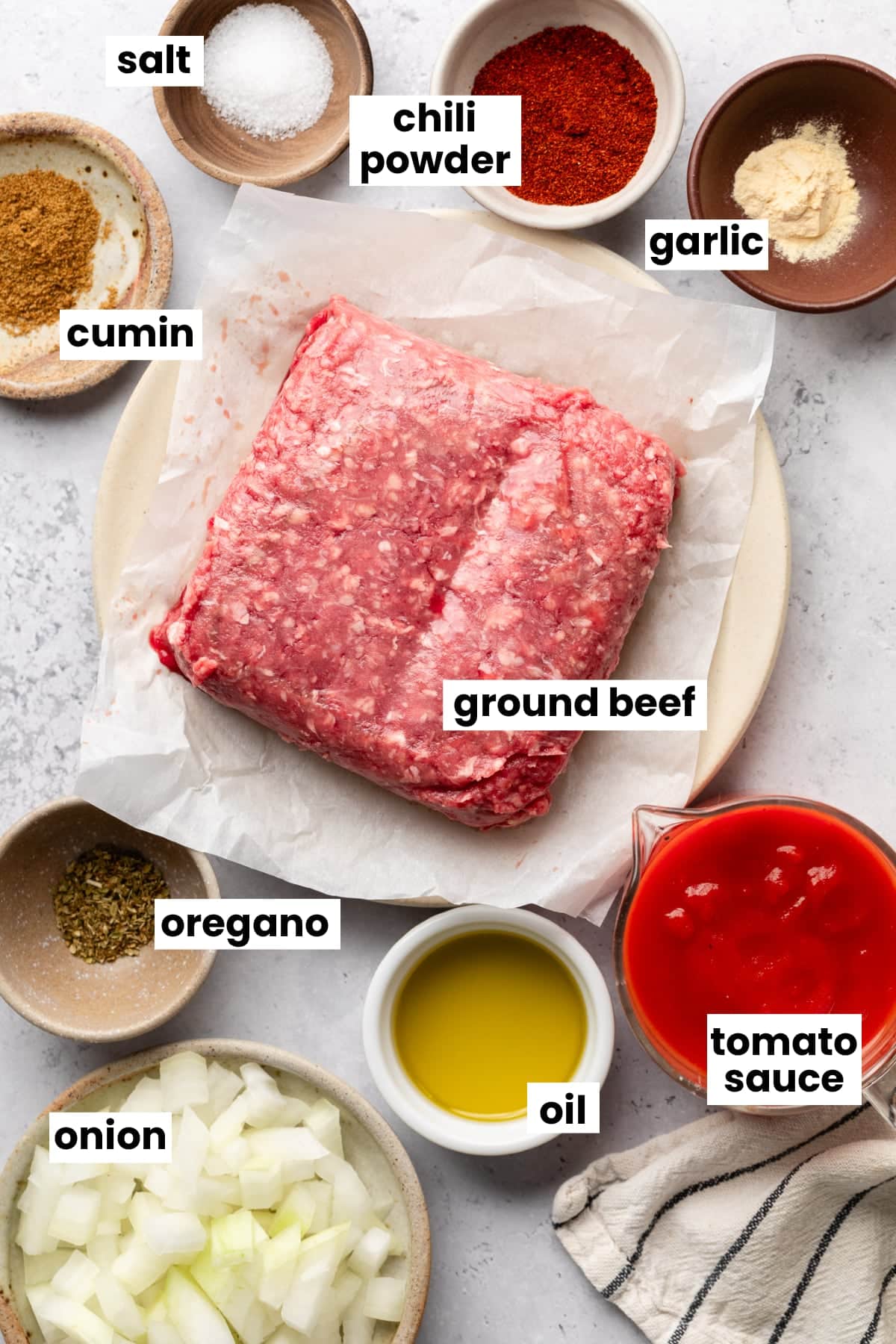 Ingredients in the recipe, including ground beef, cumin, salt, chili powder, garlic, oregano, oil, tomato sauce, and onion.