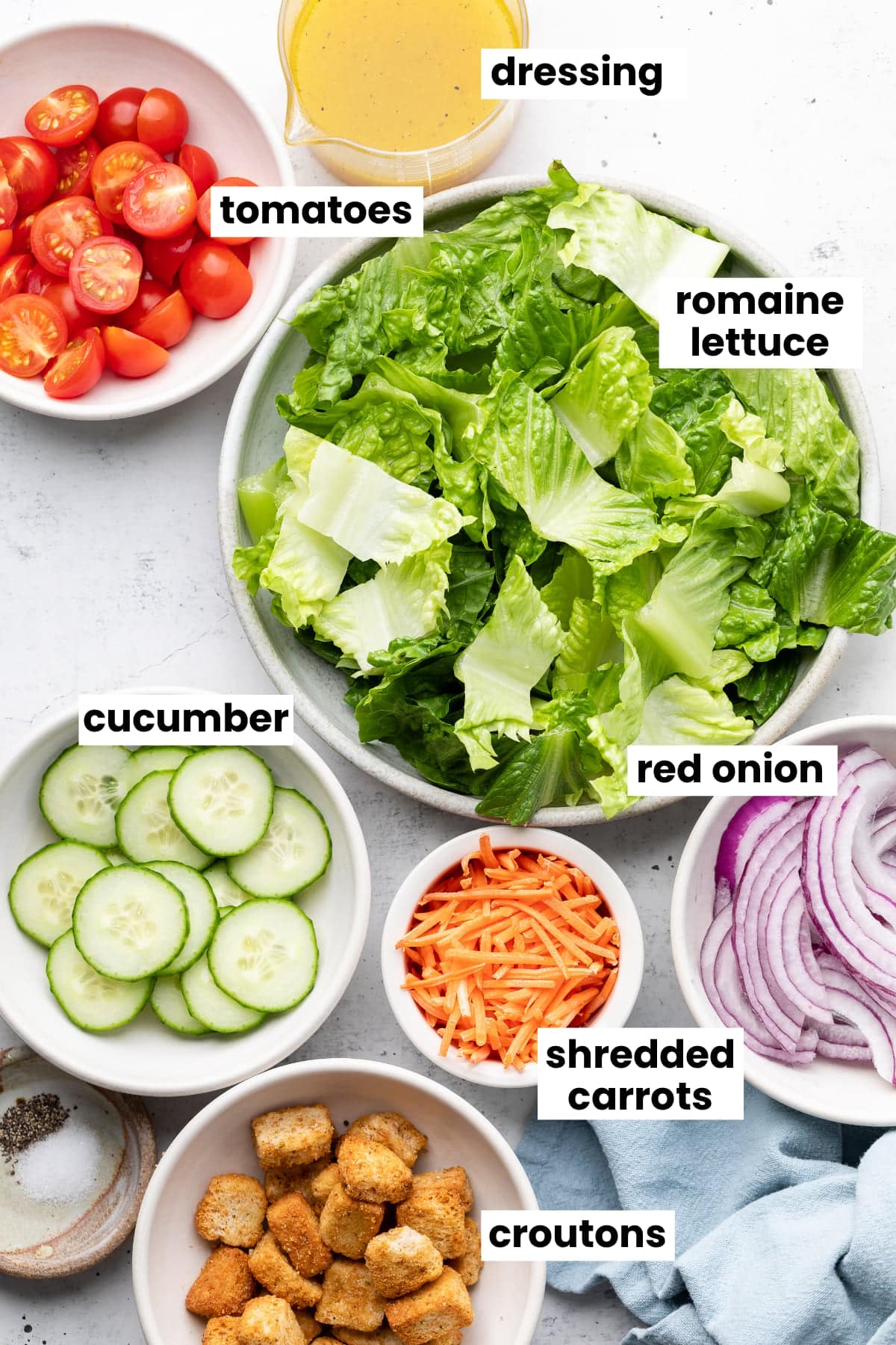 Ingredients in the house salad recipe, including cucumber, red onion, romaine lettuce, tomatoes, shredded carrots, dressing, and croutons. 