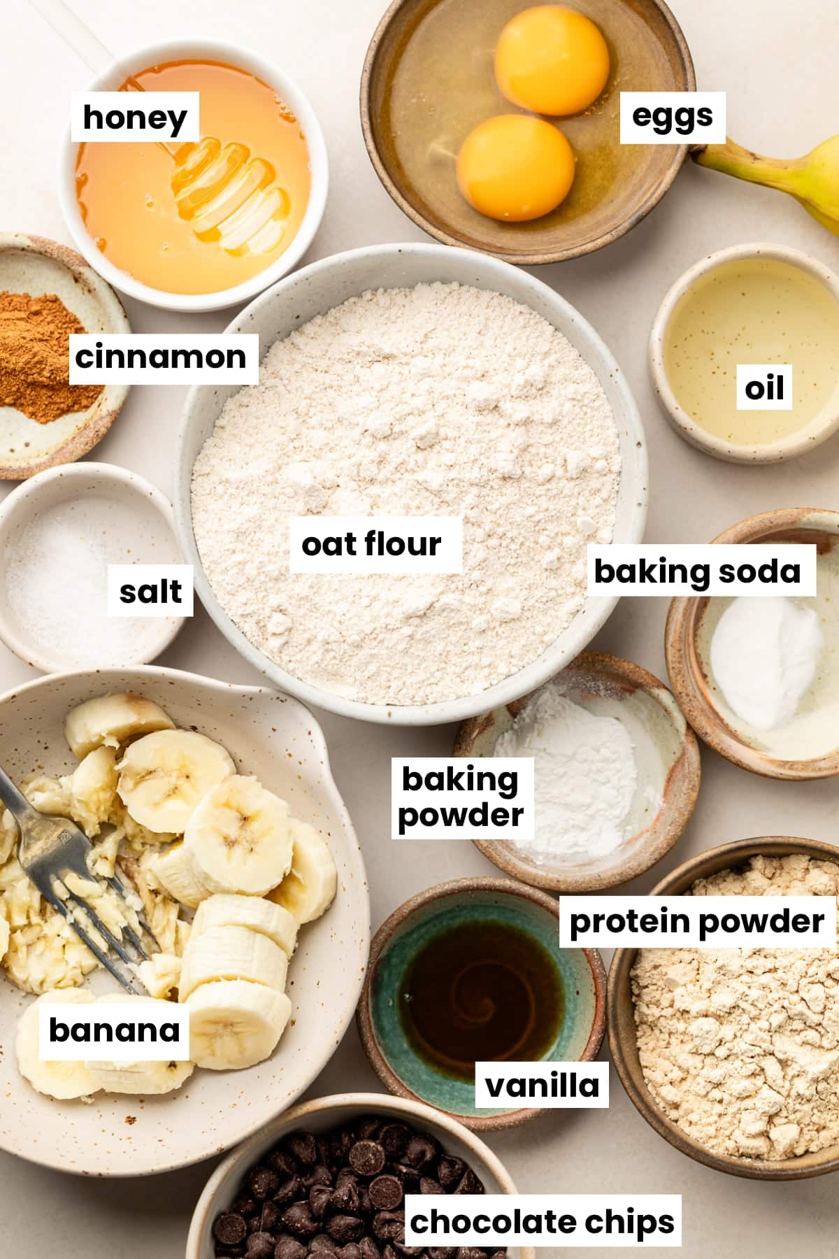 Ingredients in the recipe, including bananas, protein powder, oat flour, oil, cinnamon, eggs, honey, baking powder, baking soda, vanilla, and chocolate chips.