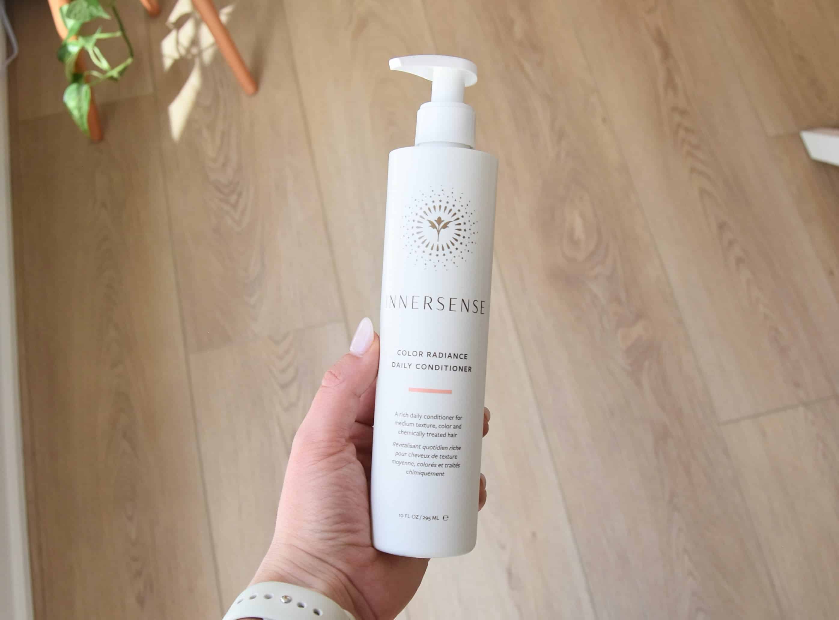 Holding a bottle of the Innersense Color Radiance Daily Conditioner.