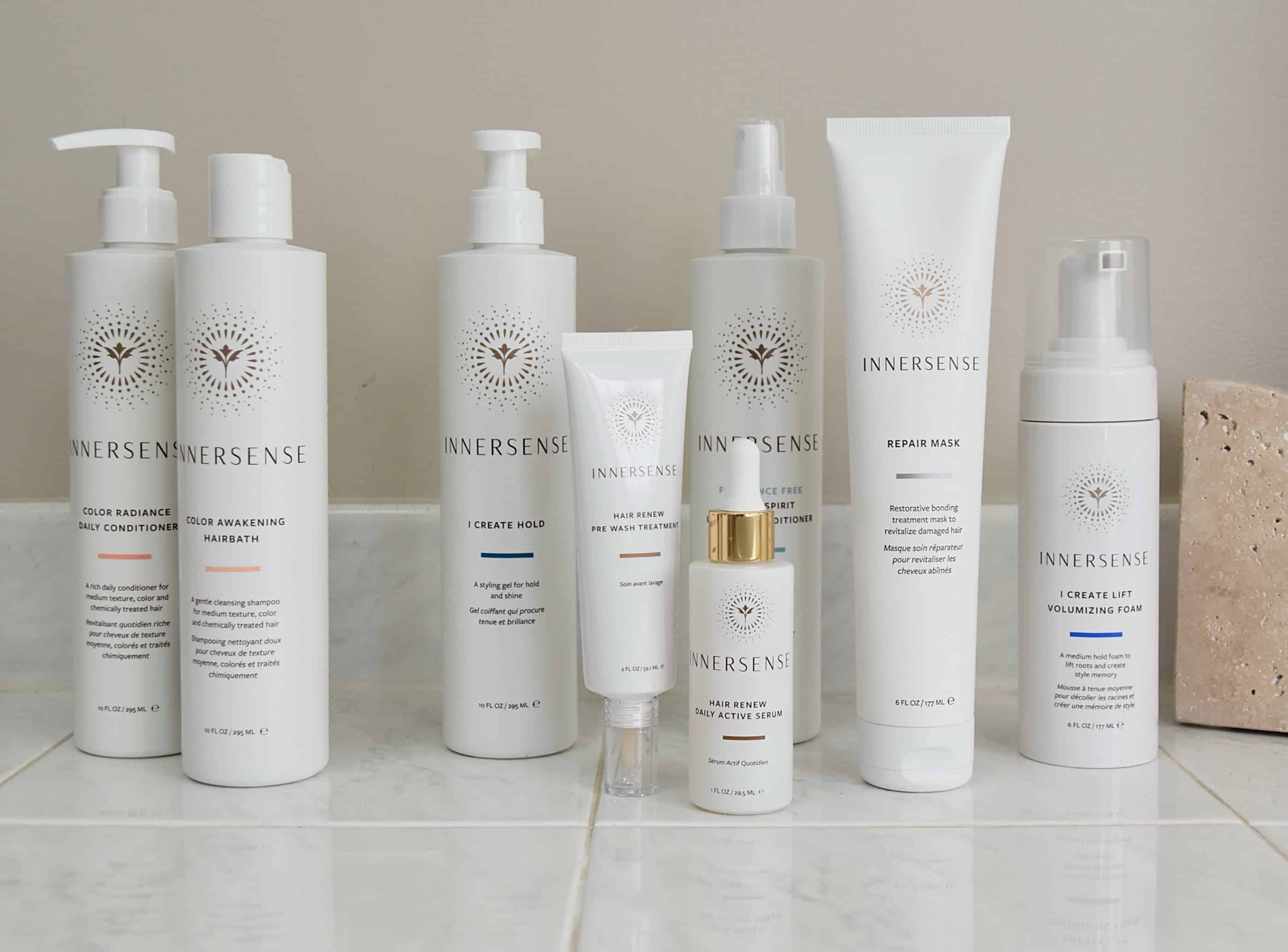 All of the innersense hair products listed in the review on the bathroom counter, including: Color Awakening Hairbath, Color Radiance Conditioner, I Create Hold, Hair Review Daily Active Serum, Hair Renew Pre Wash Treatment, Repair Mask, Leave In Conditioner, and the I Create Lift Foam.
