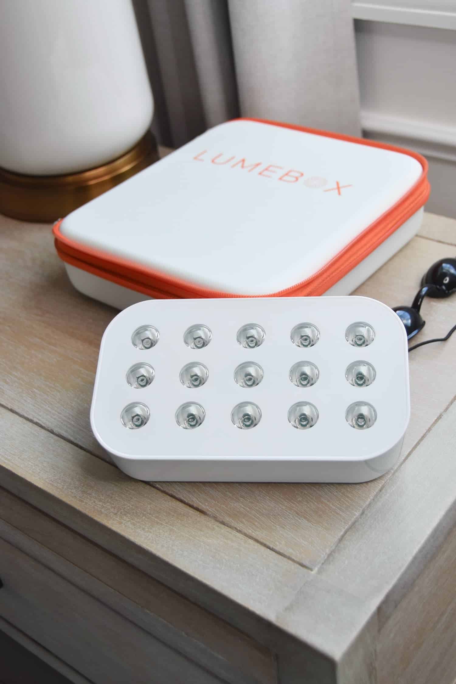 A lumebox device sitting on a nightstand with the carrying case and goggles.